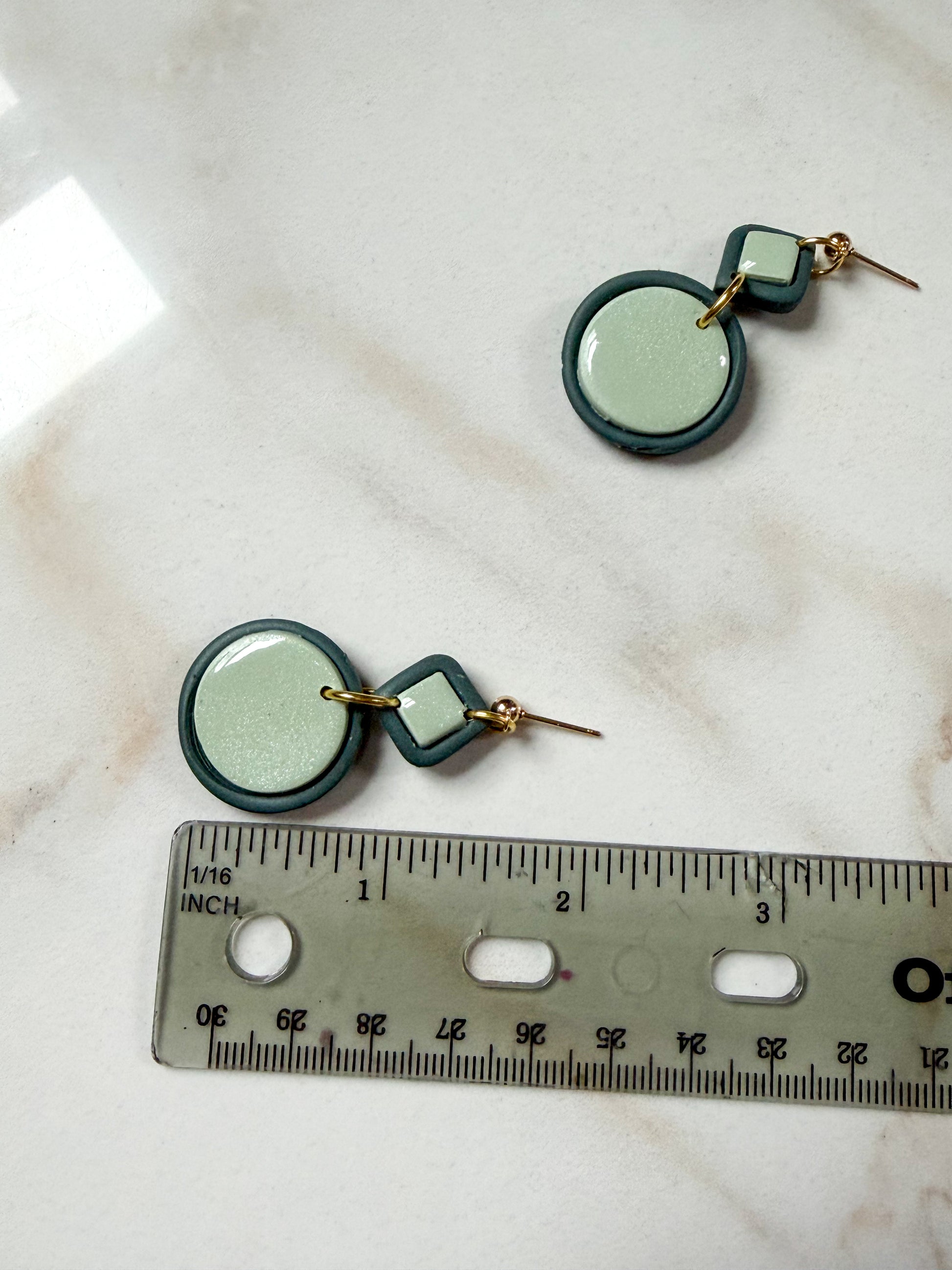 Green circular earrings on a marble surface with a ruler for scale. About 1 and 3/4 inches long. 