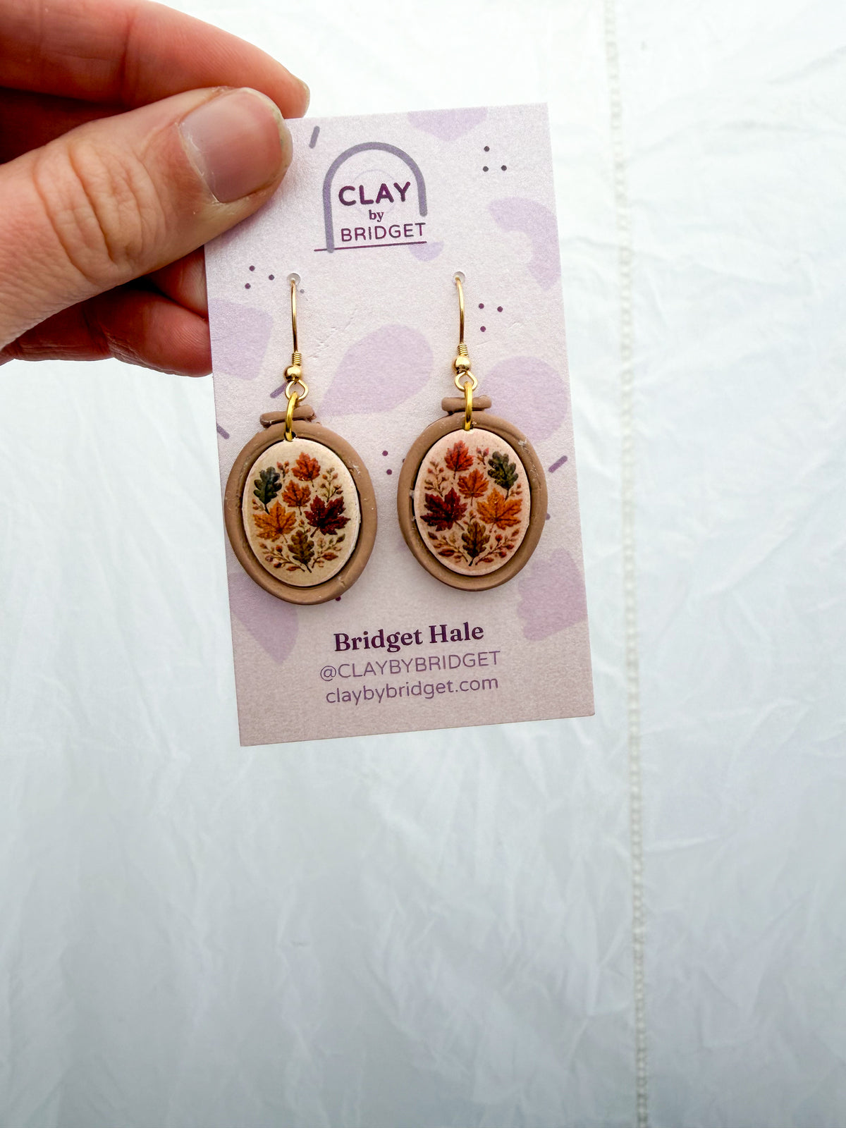 Embroidery hoop shaped earrings with a fall leaf design inside.