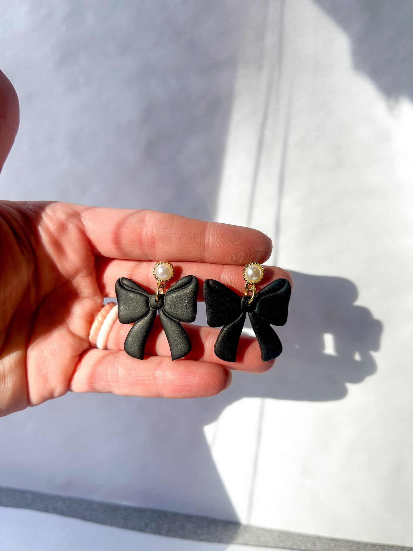 Black bow-shaped earrings held in a hand against a light background