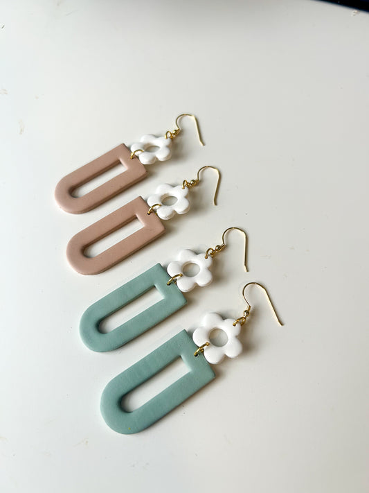 Two pairs of earrings on a white background. One pair is brown and the other is green. It’s an upside down window cutout shape, with a white daisy donut shape on top. Hook posts. 