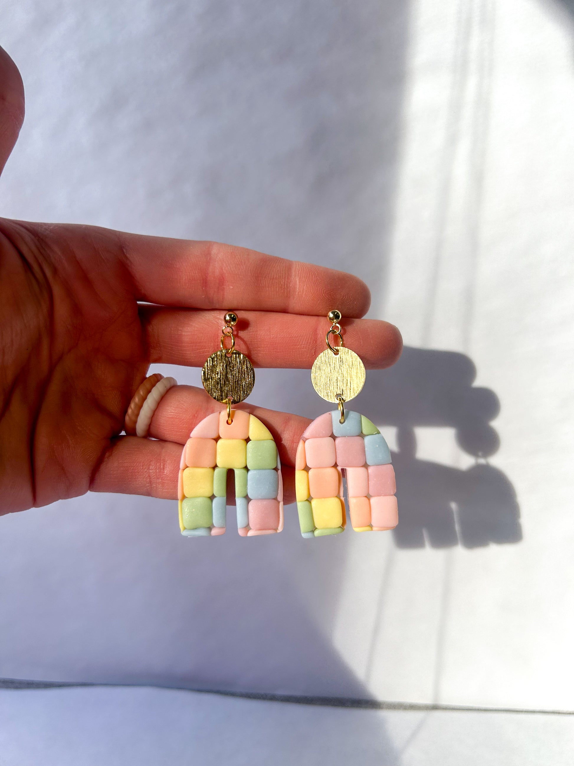 Pastel rainbow-shaped earrings held by a hand on a white background