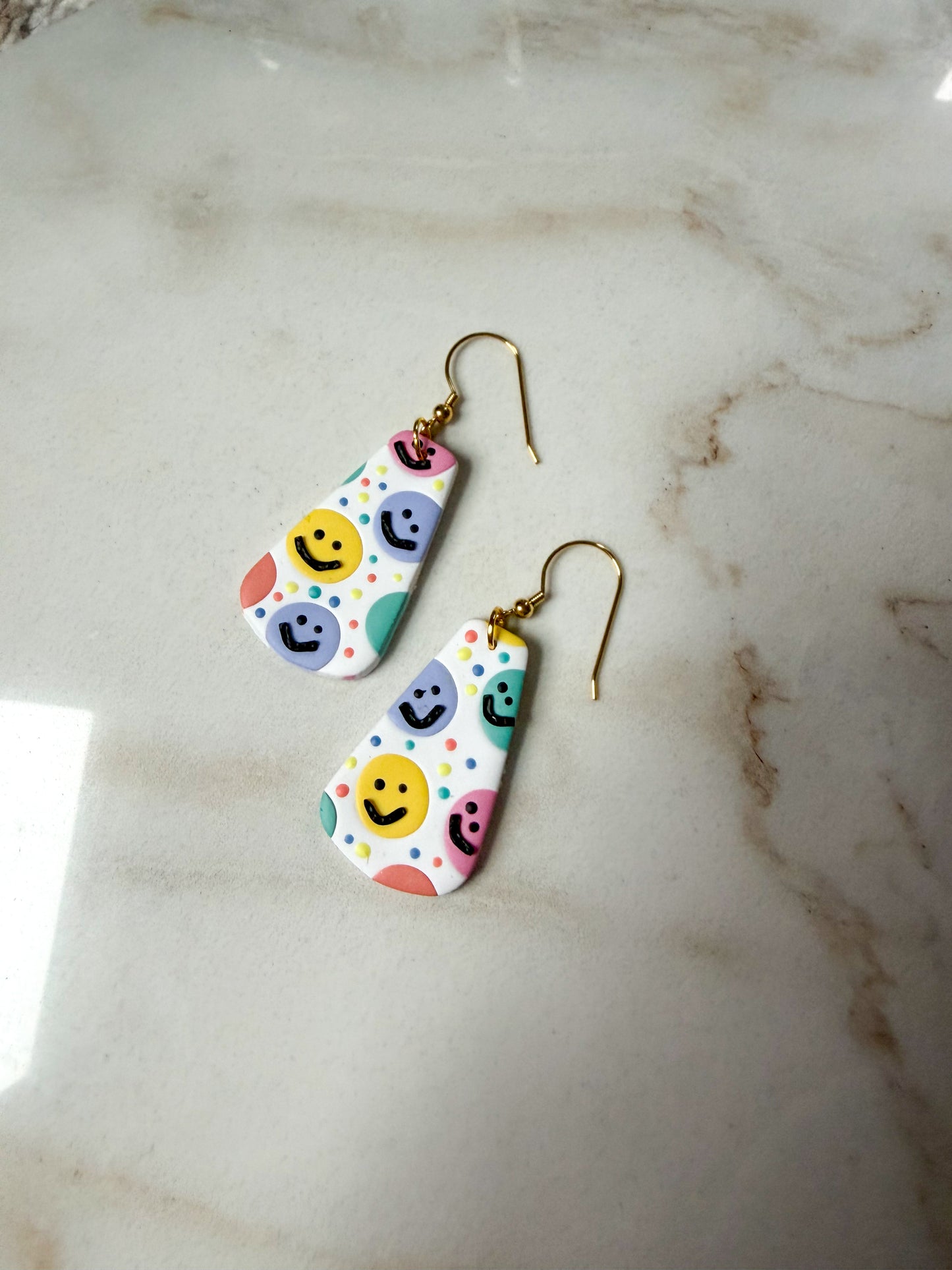 Colorful smiley face earrings on a marble surface
