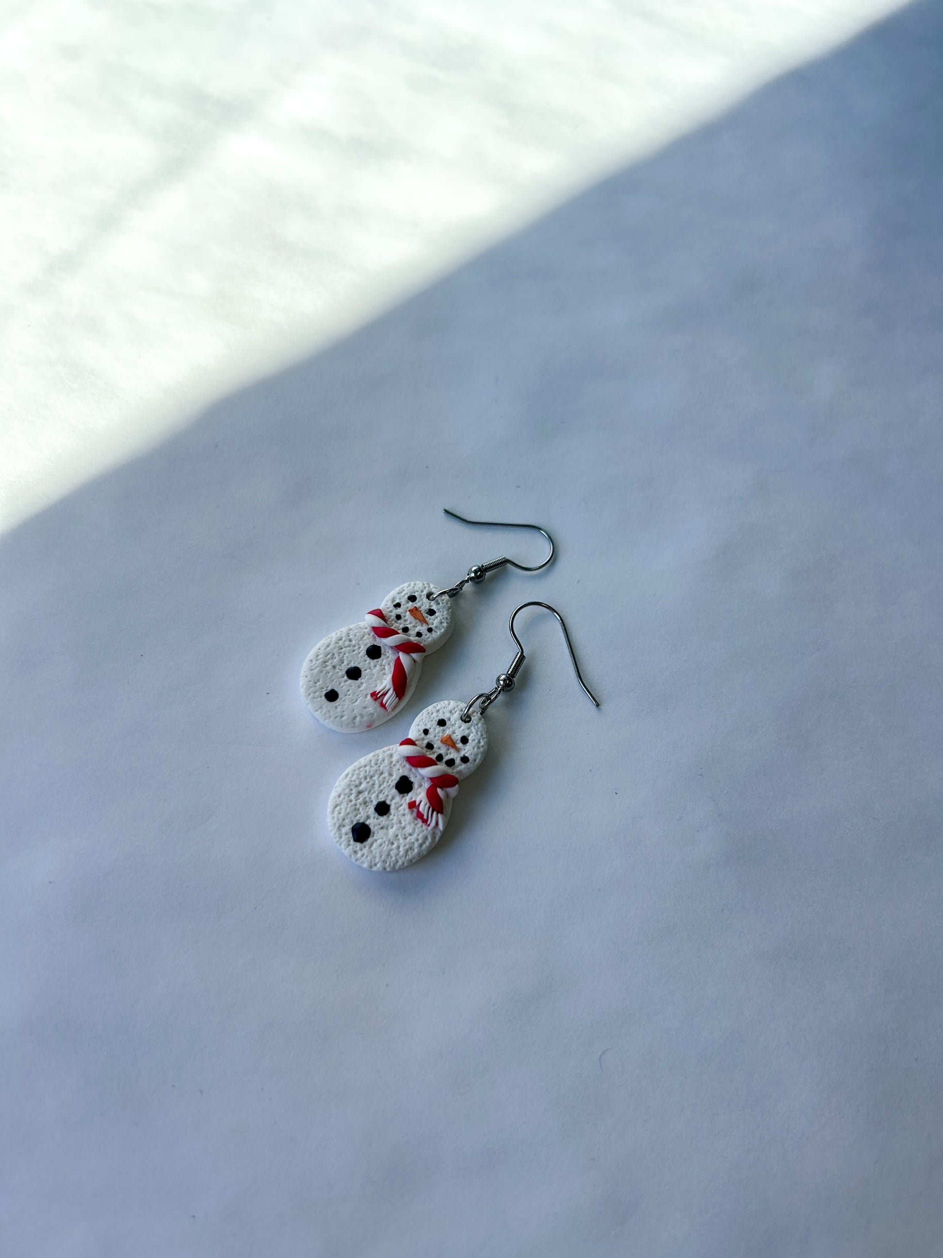 Snowman-shaped earrings on a light background. 