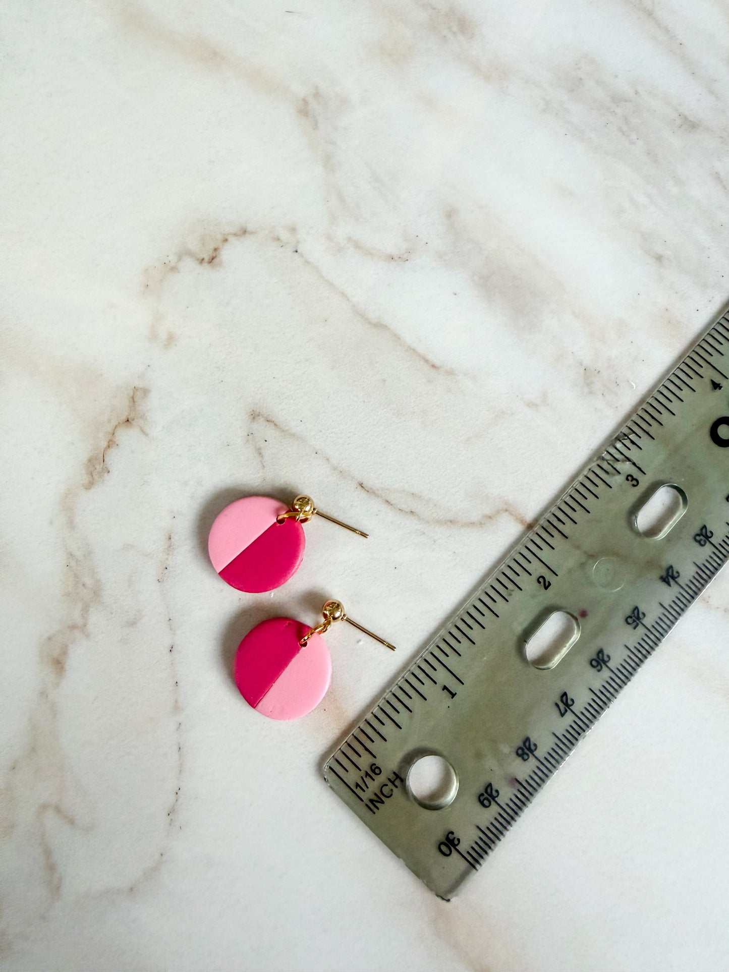 Pink and gold earrings on a marble surface with a ruler for scale. About one inch in length 