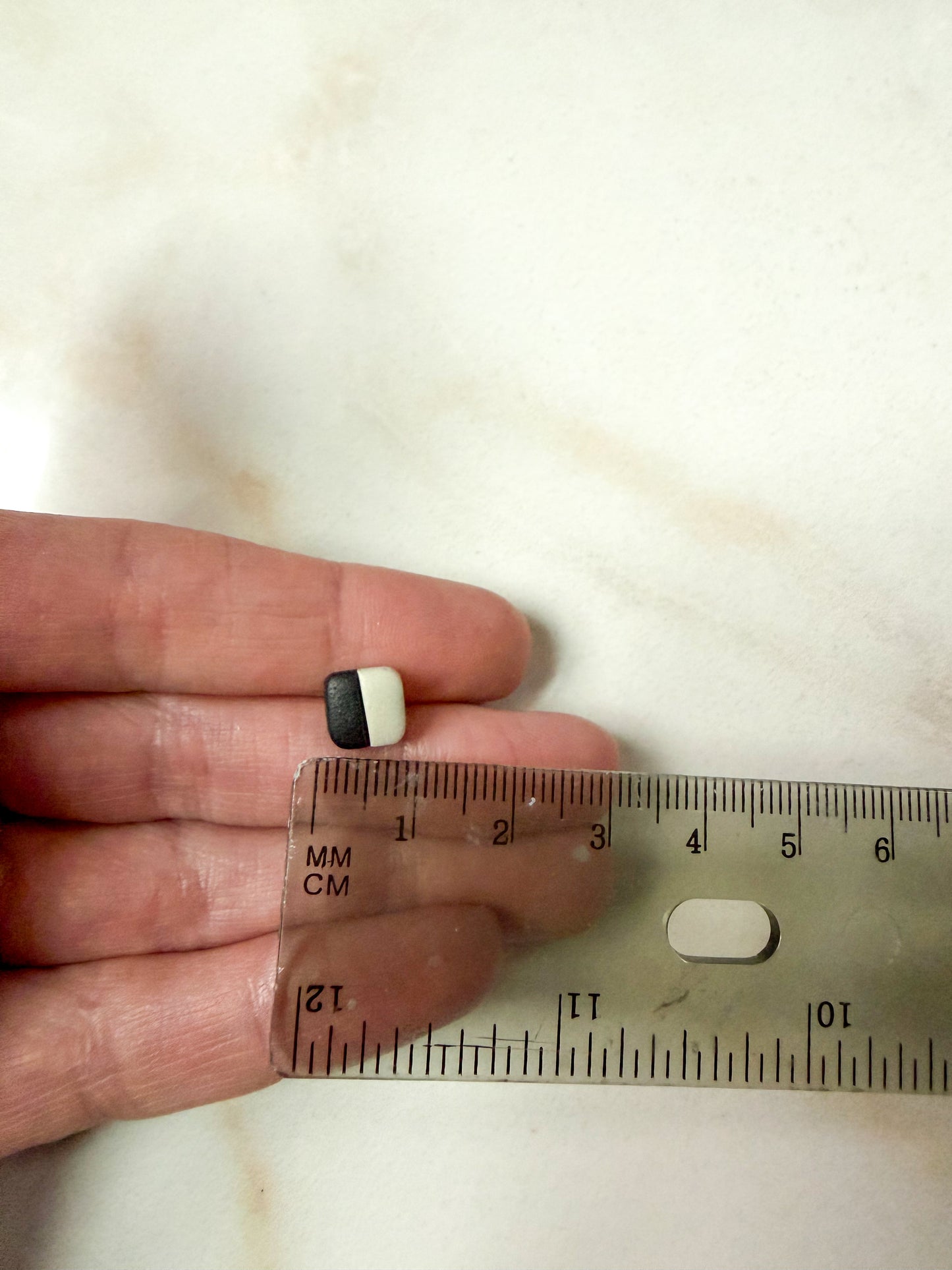 Small square studs in front of a ruler for scale. Less than 1 cm in length