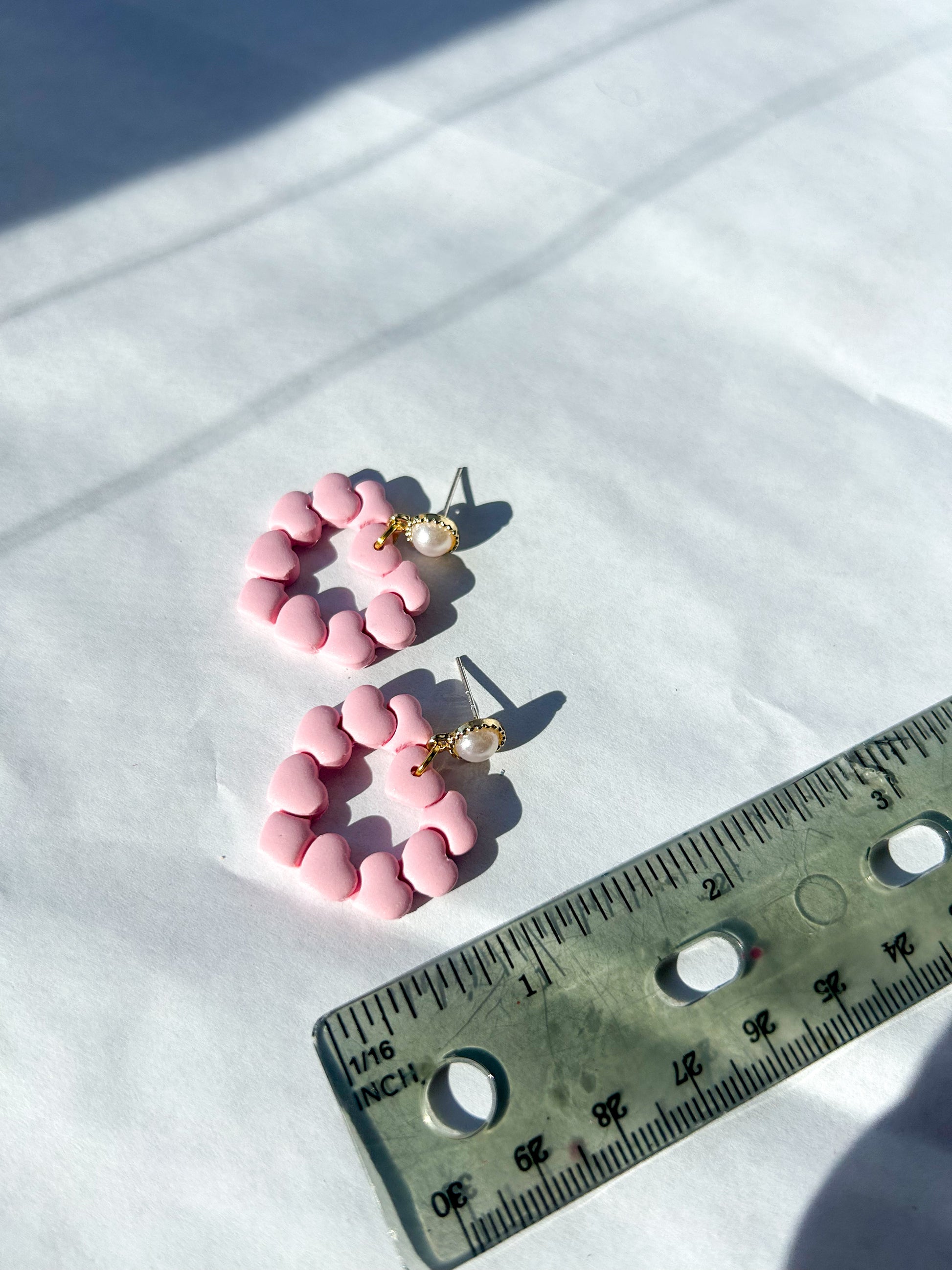 Pink earrings on a white surface with a ruler for scale. About 2.25 inches 