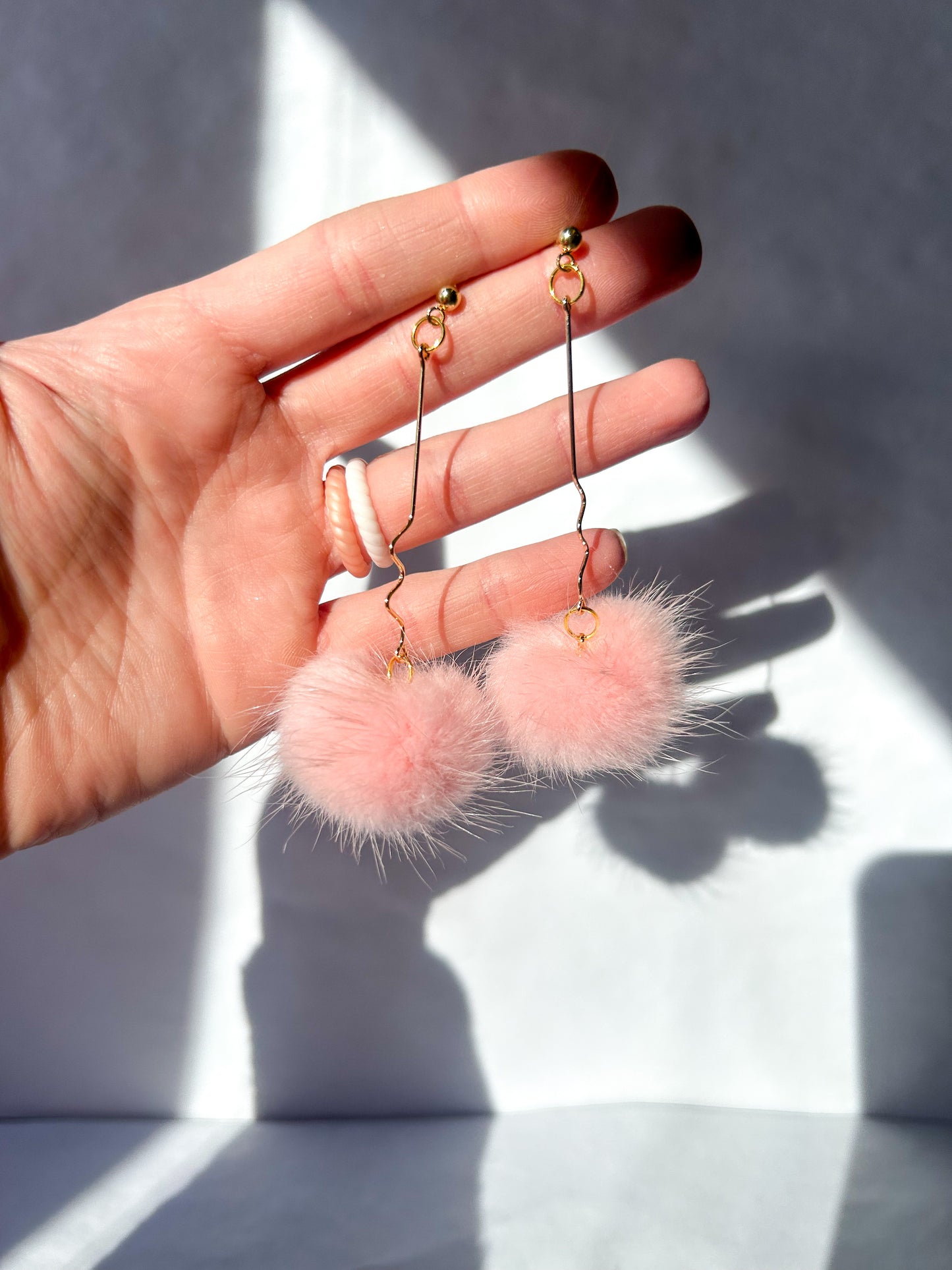 Hand holding pink fuzzy earrings with a neutral background