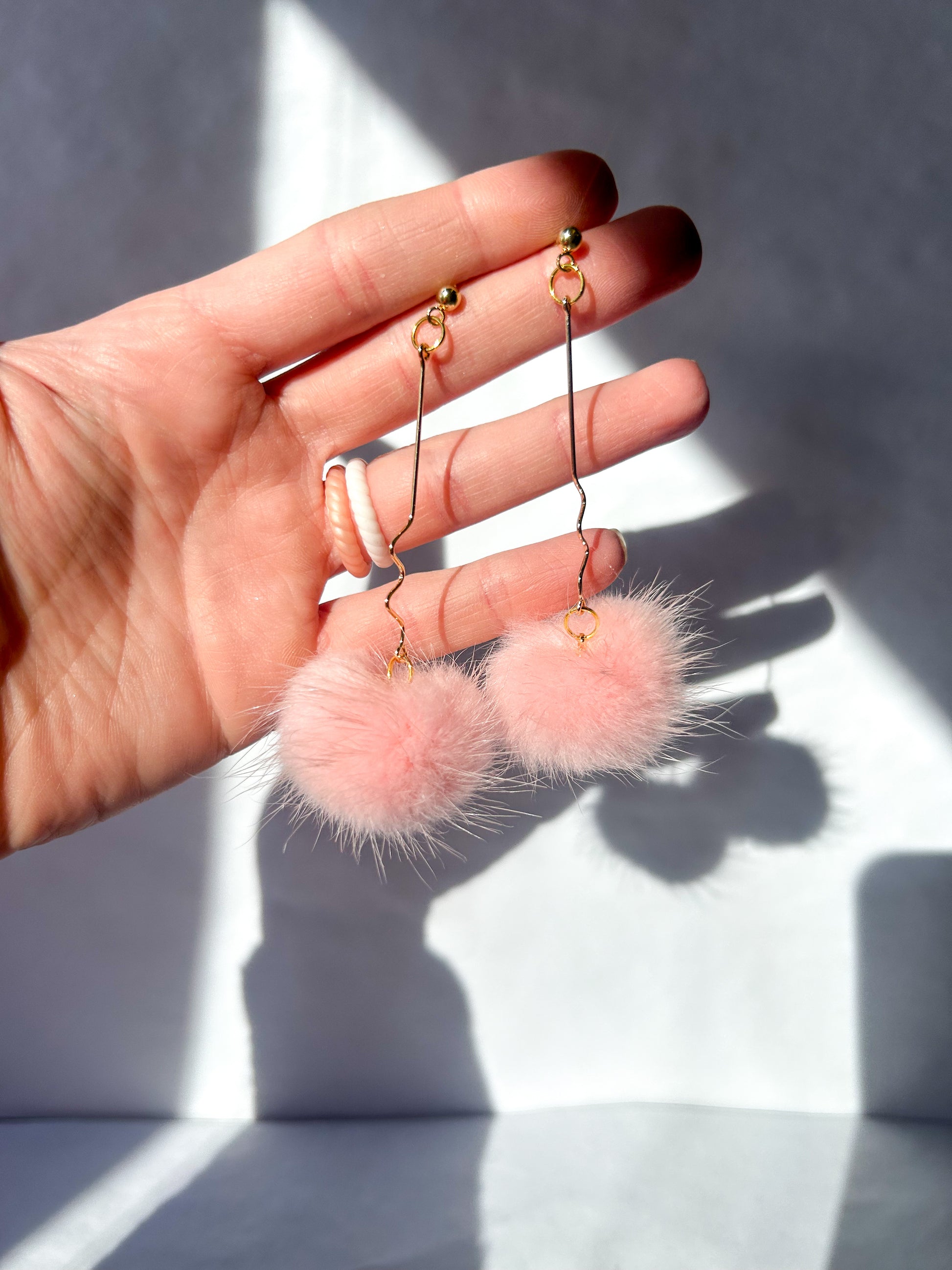 Hand holding pink fuzzy earrings with a neutral background