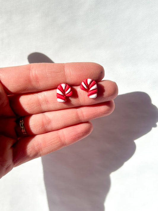 Red and white striped earrings held between fingers against a white background. Earrings look like tiny candycane studs 