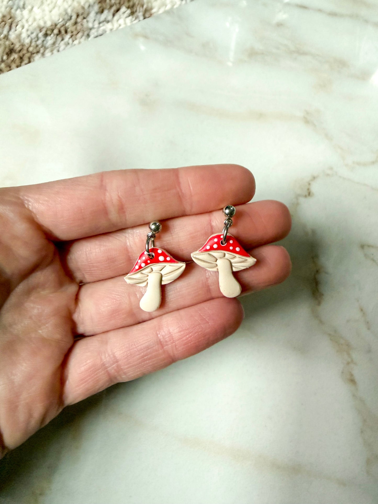Mushroom-shaped earrings held in a hand on a marble surface