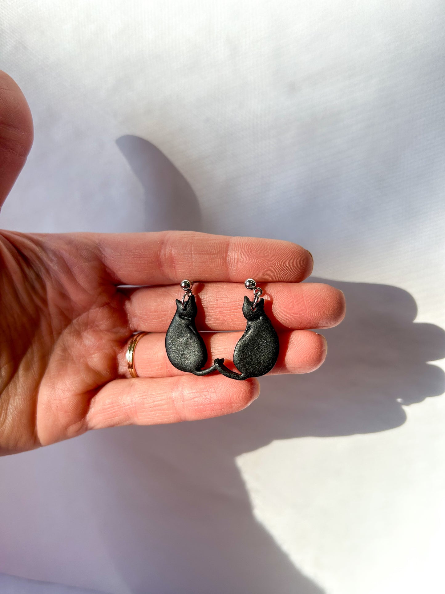 Black cat-shaped earrings held in a hand against a white background