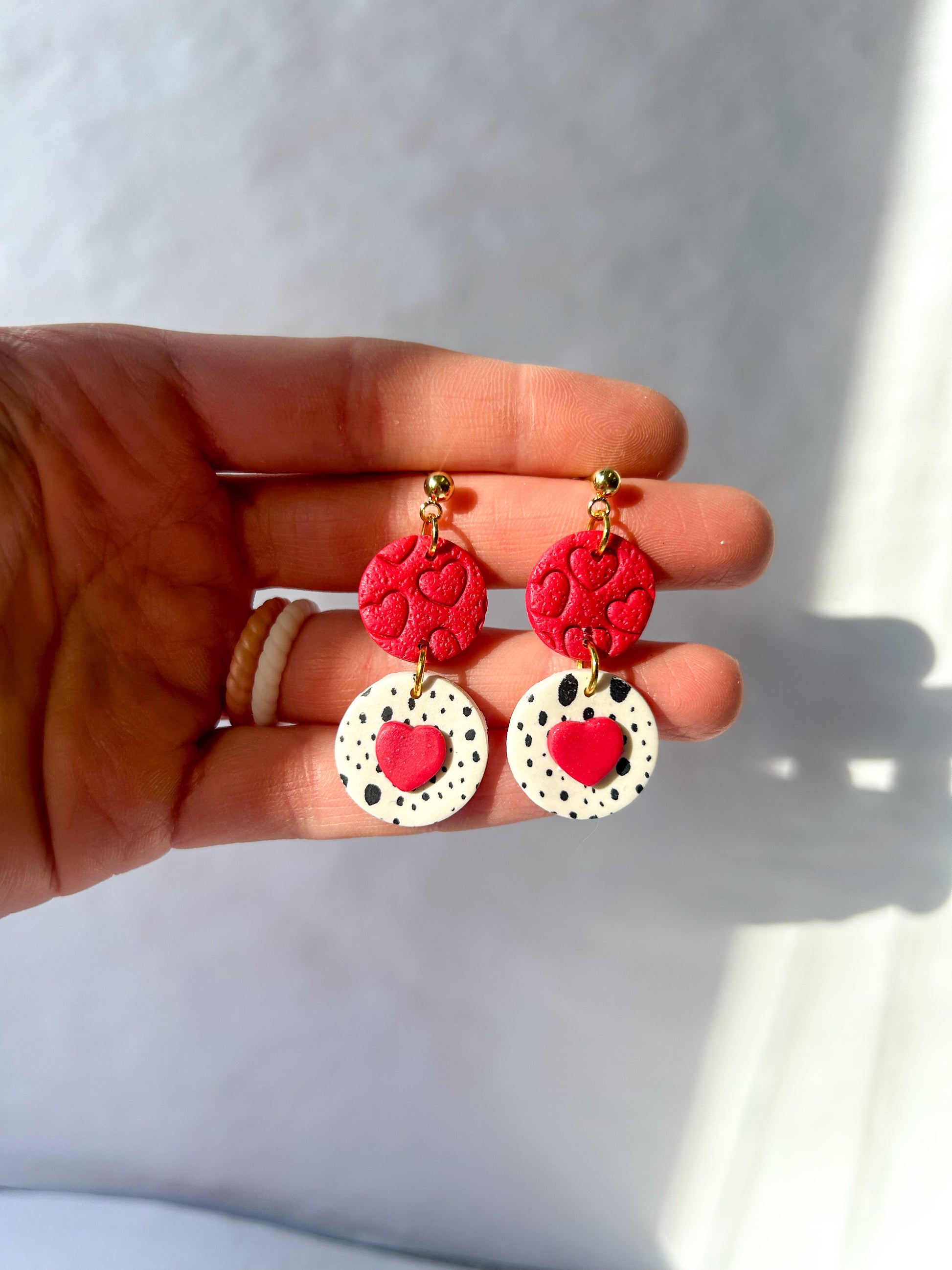 Hand holding a pair of red and white earrings against a white background