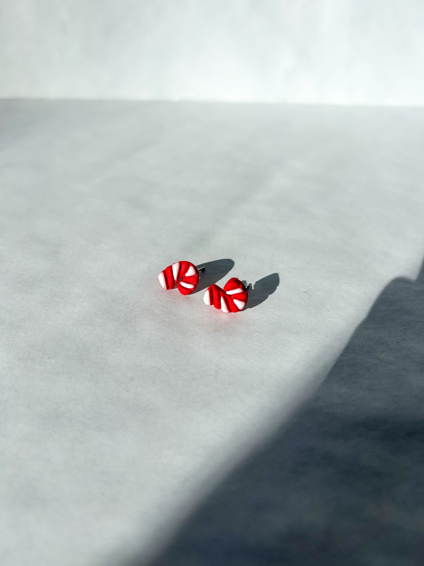 Red and white earrings on a light surface. Earrings resemble tiny candy canes. 