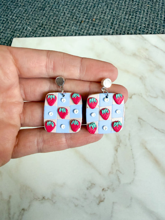 Hand holding a pair of earrings with strawberry design on a marble surface