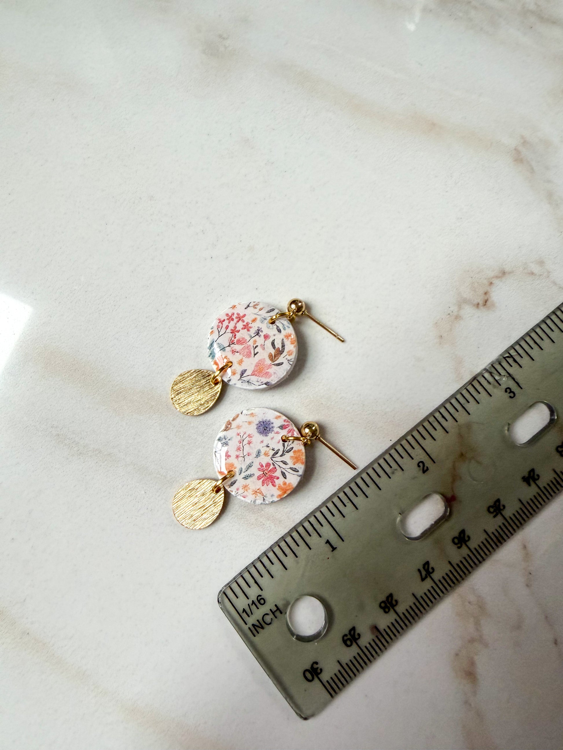 Floral earrings on a marble surface with a ruler for scale. About 1.5 inches long. 