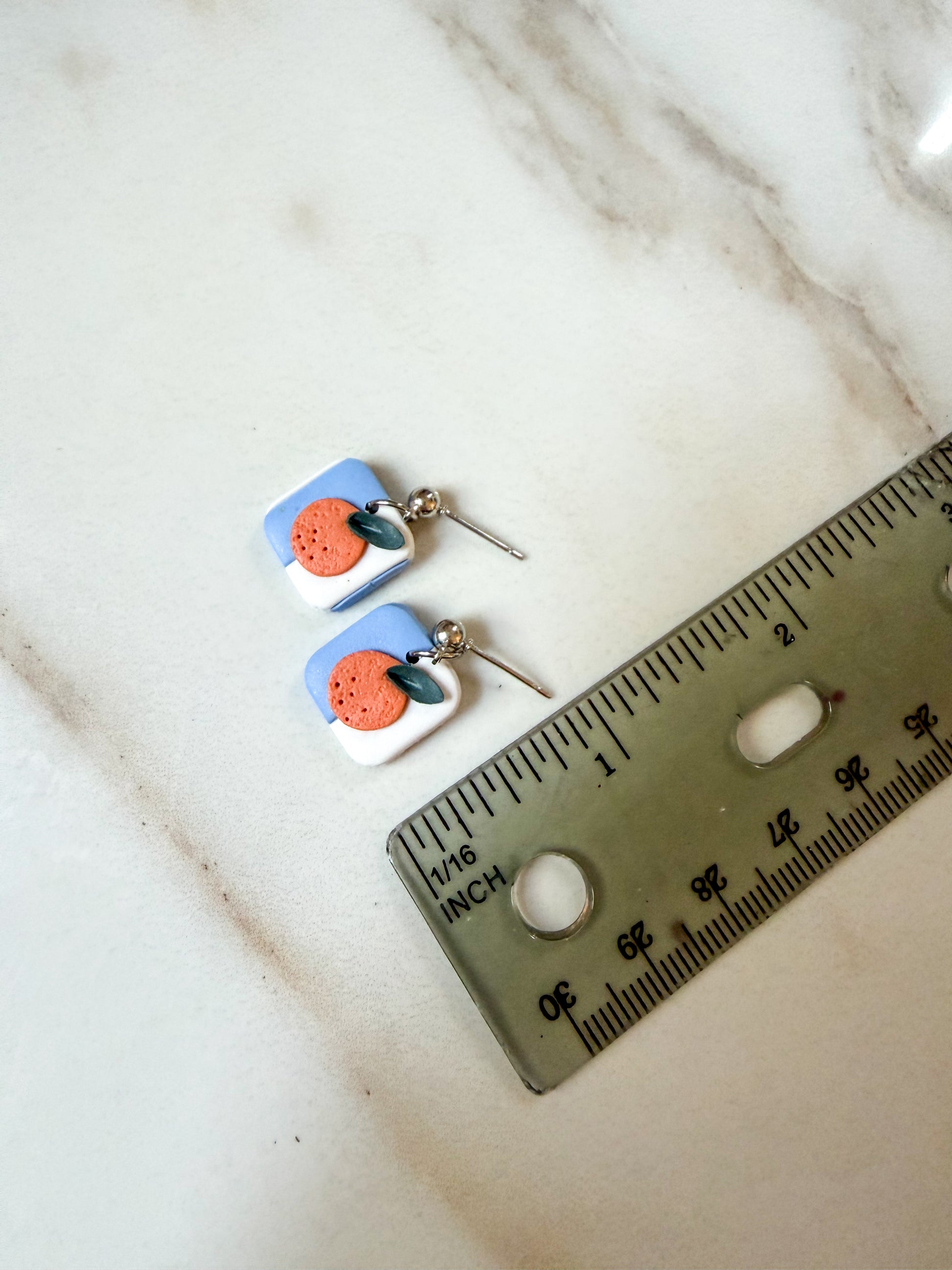 A pair of small blue and white earrings with an orange in the center. About 3/4 inches long. 
