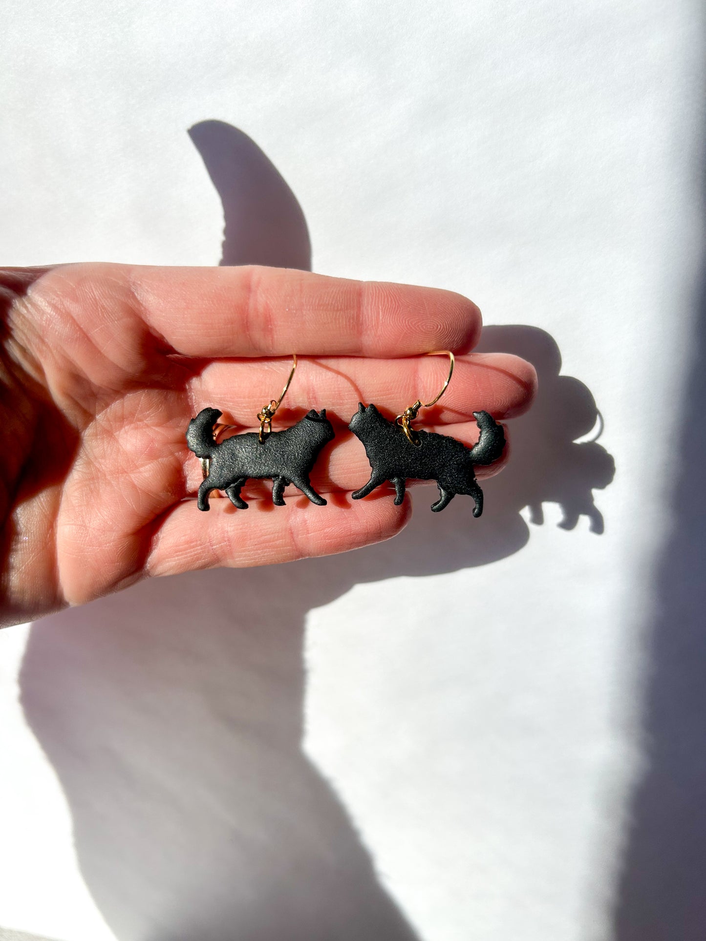 Hand holding long haired black cat-shaped earrings against a white background