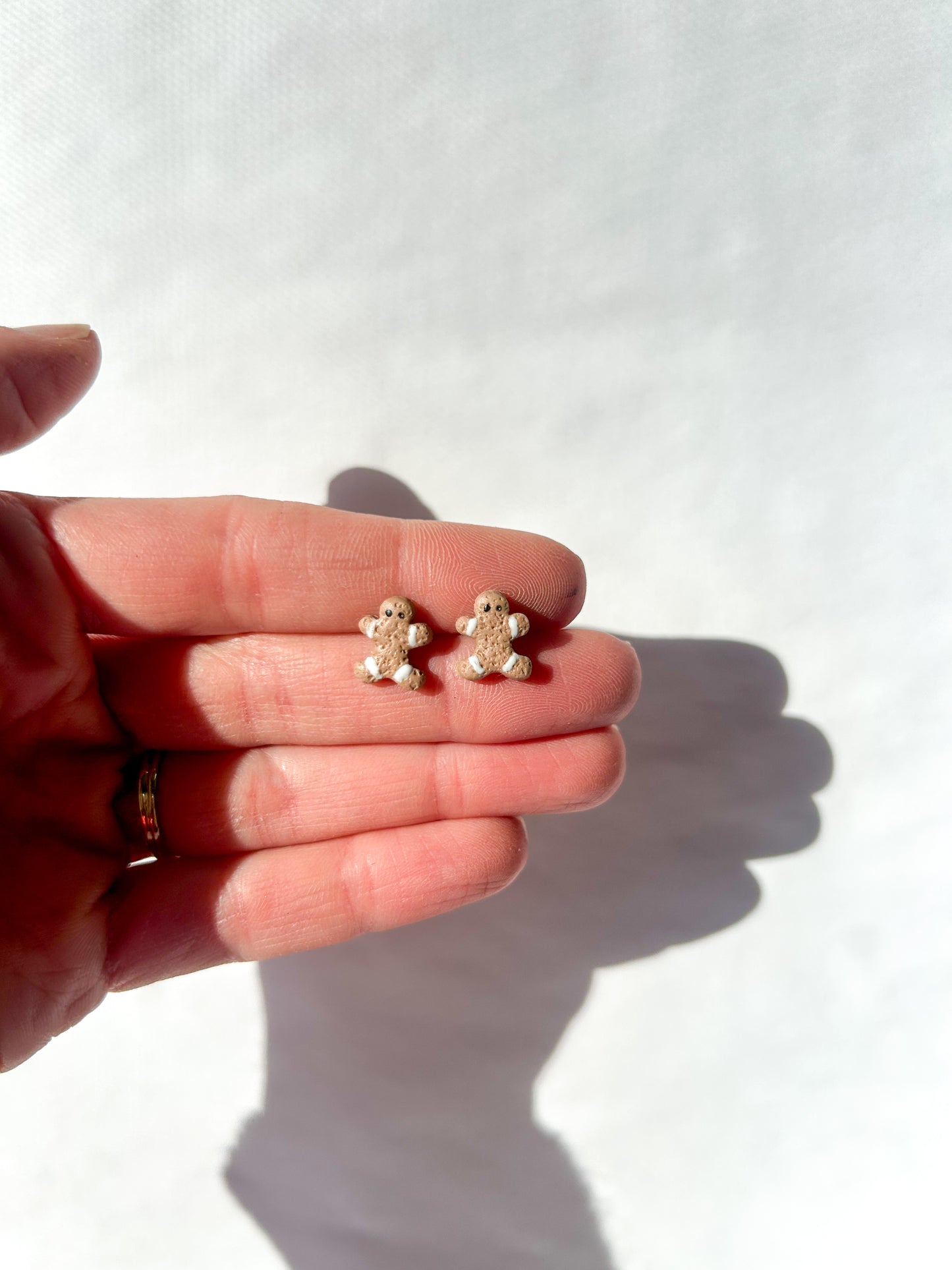 Small gingerbread man shaped earrings held between fingers on a white background