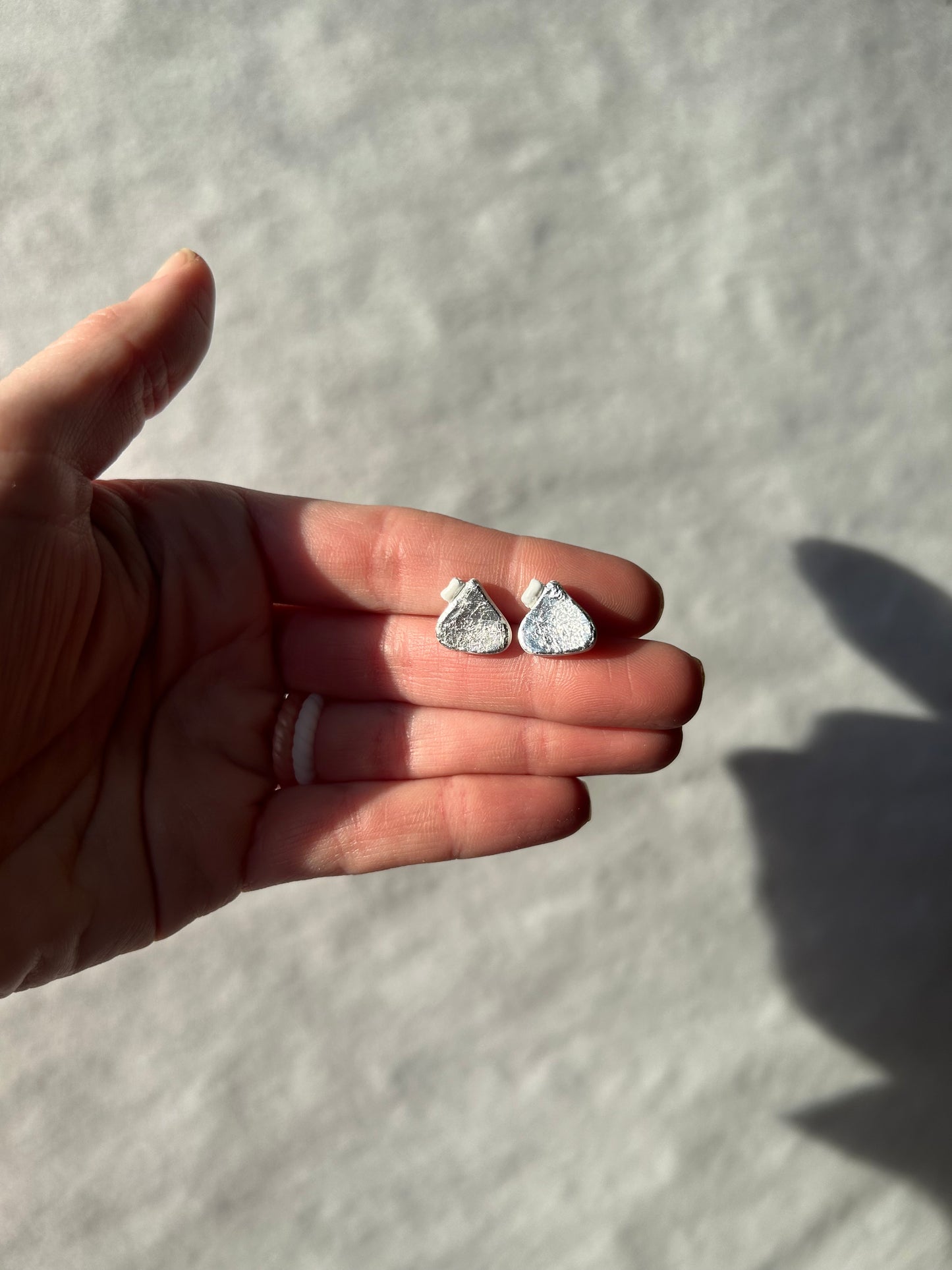 Hand holding two silver earrings against a light background