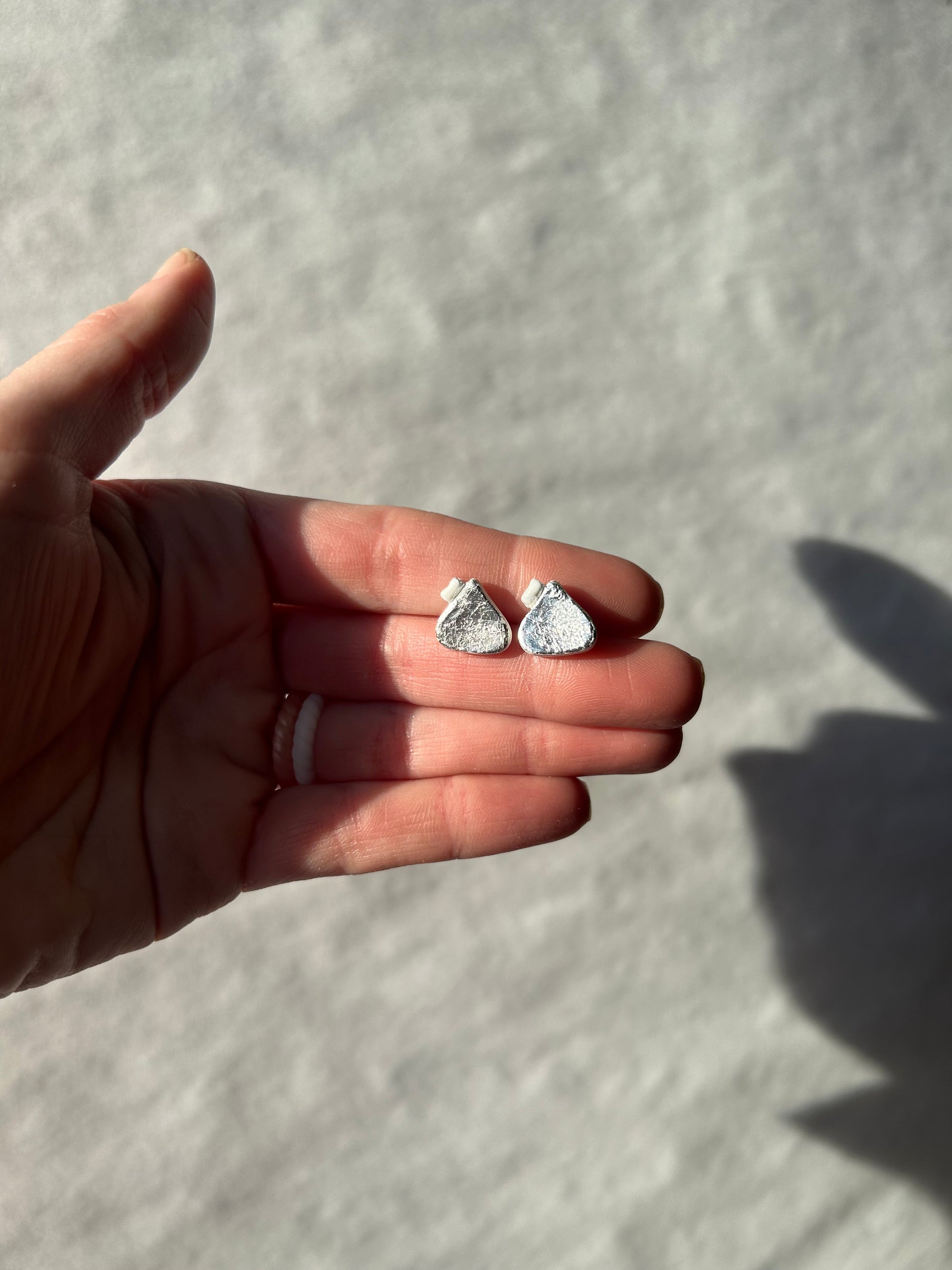 Hand holding two silver earrings against a light background