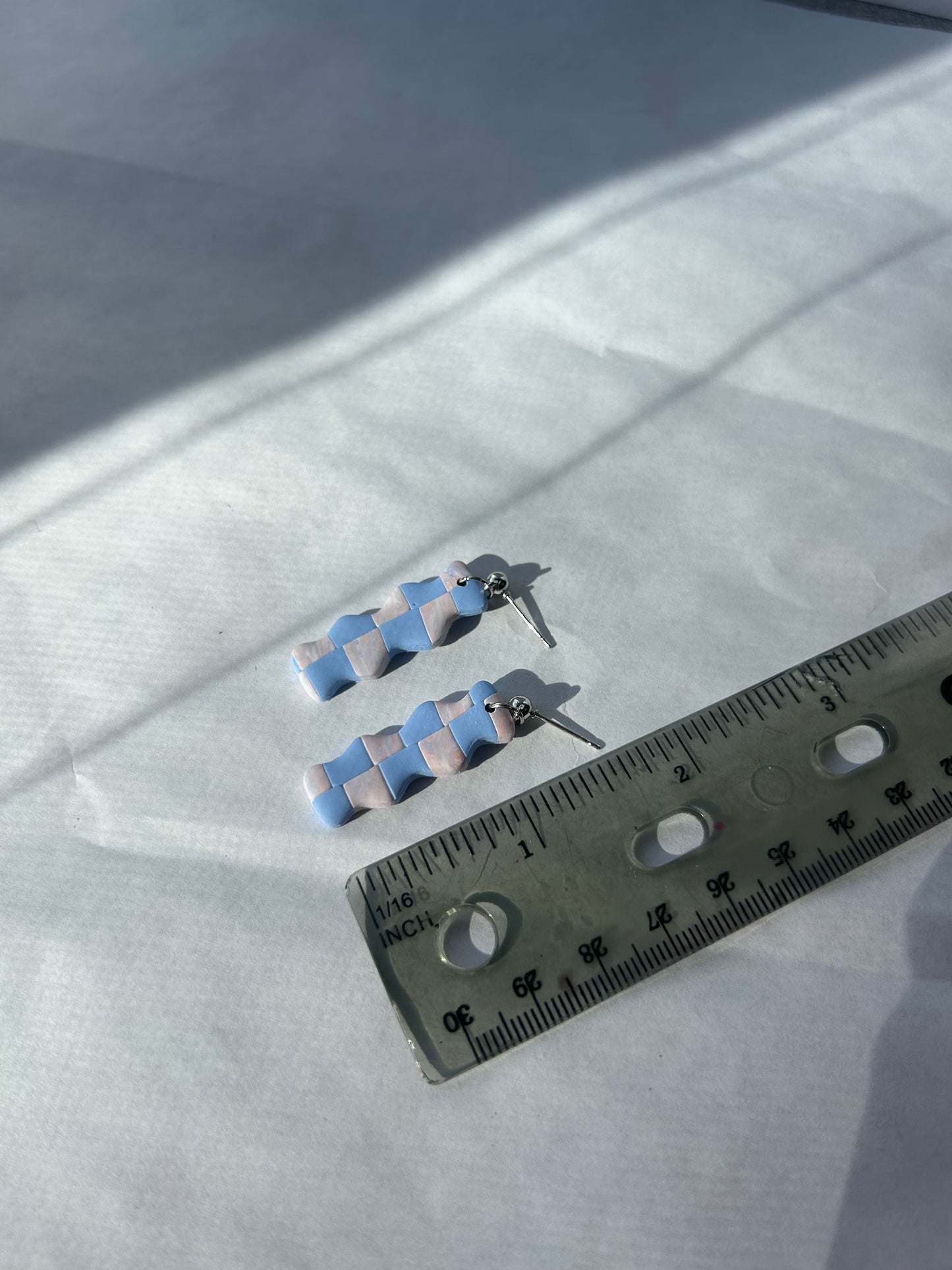 Pair of earrings with a ruler for scale on a white fabric background. 1 1/2 inches long