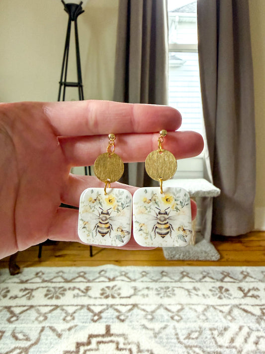 Earrings with a bee design In a hand against a neutral background
