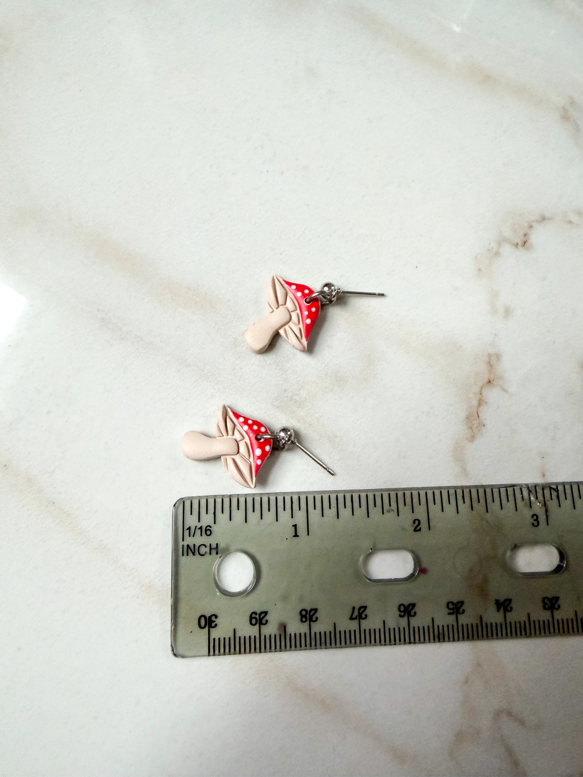 Two mushroom-shaped earrings on a marble surface with a ruler for scale. About 1 inch long. 