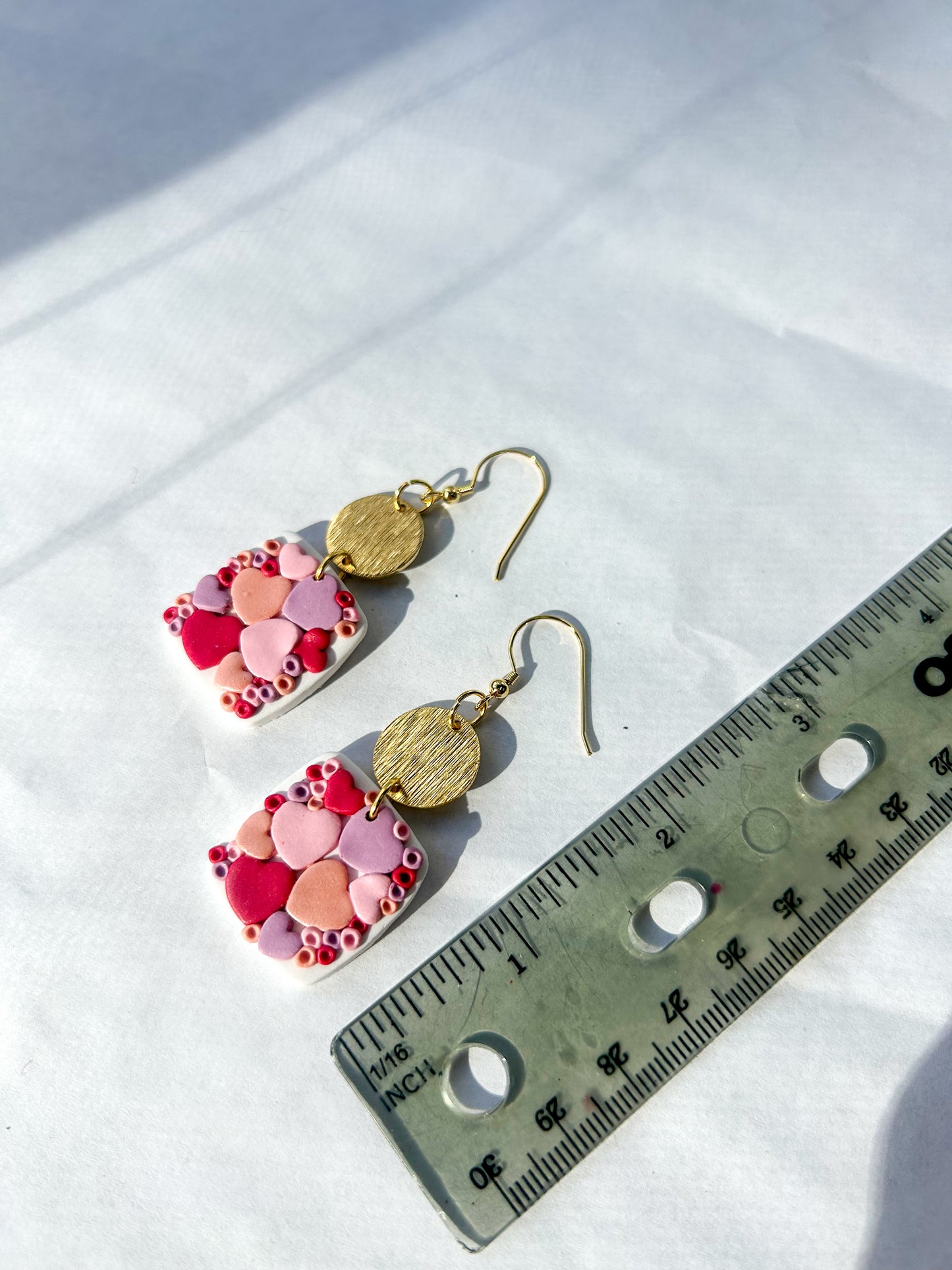 Heart-design earrings with colorful beads and gold accents on a white surface with a ruler for scale. 2.5 inches long 