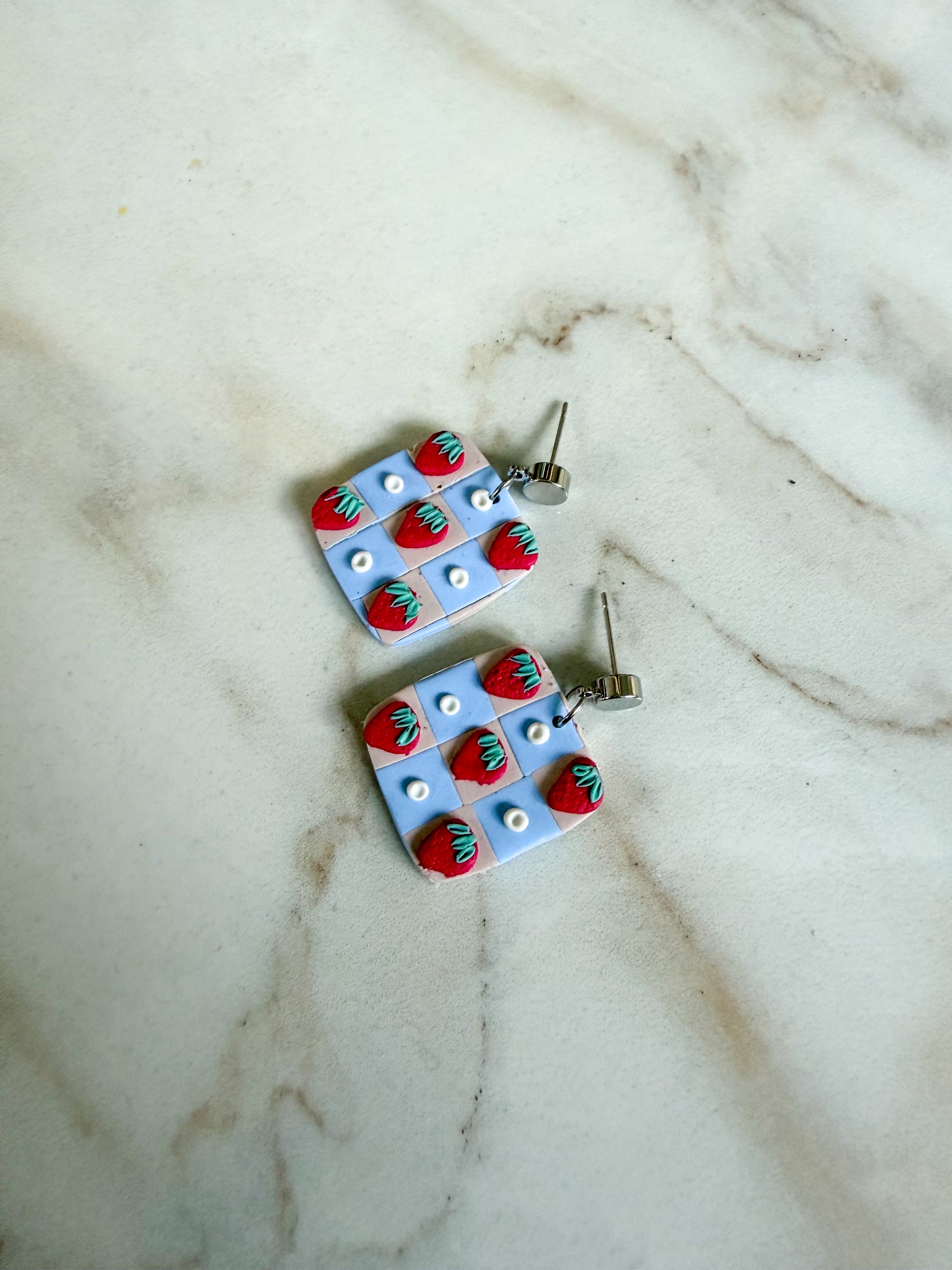 Strawberry checker earrings laying flat on a marble surface. 