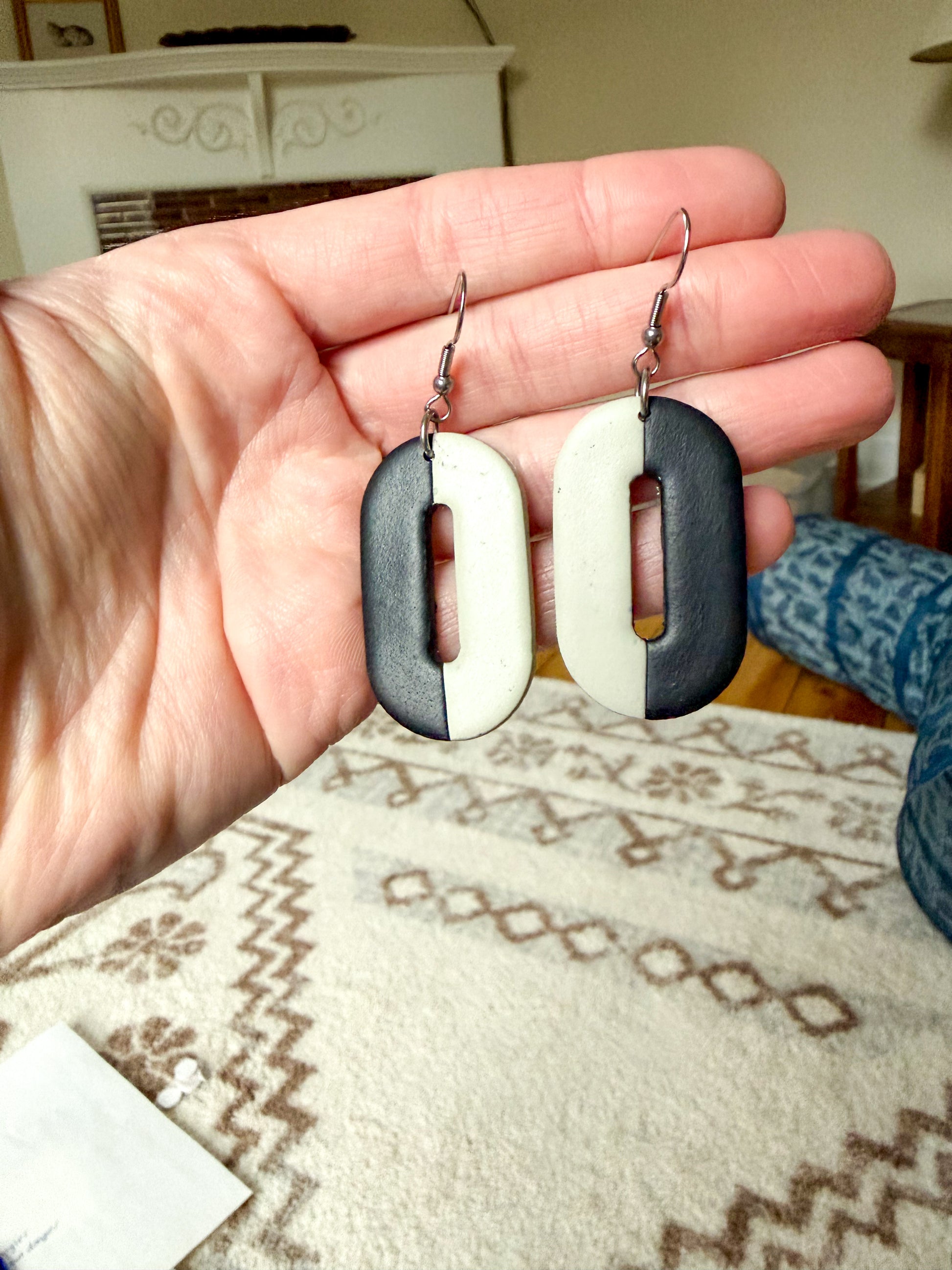 Hand holding a pair of earrings with a geometric design on a patterned rug.