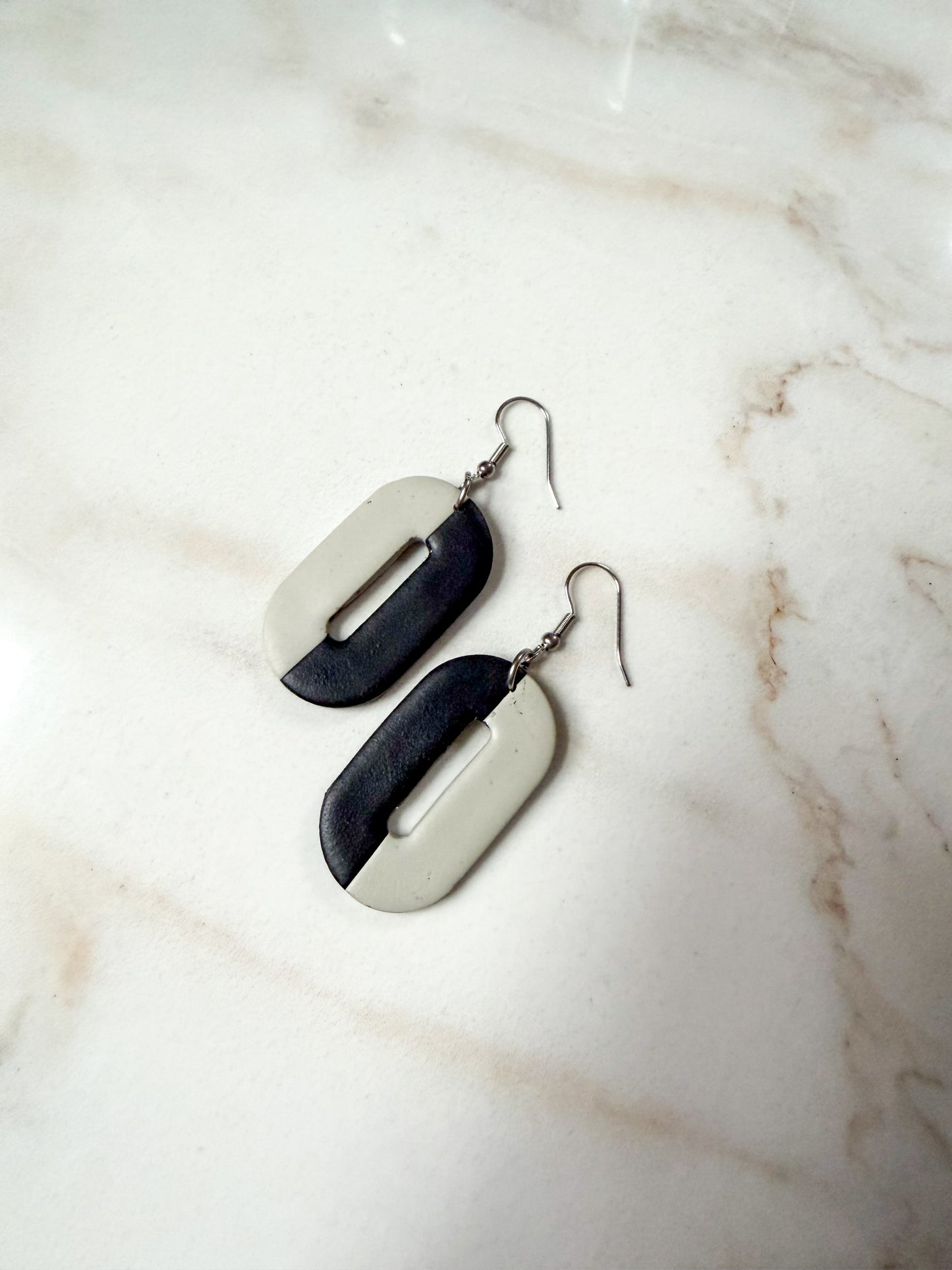 Oval earrings on a marble surface. One half is black and the other is a gray-olive color. 