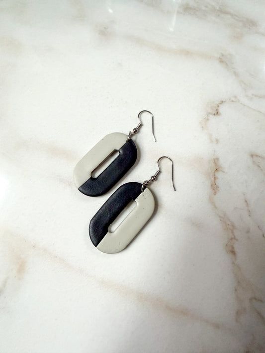 Oval earrings on a marble surface. One half is black and the other is a gray-olive color. 