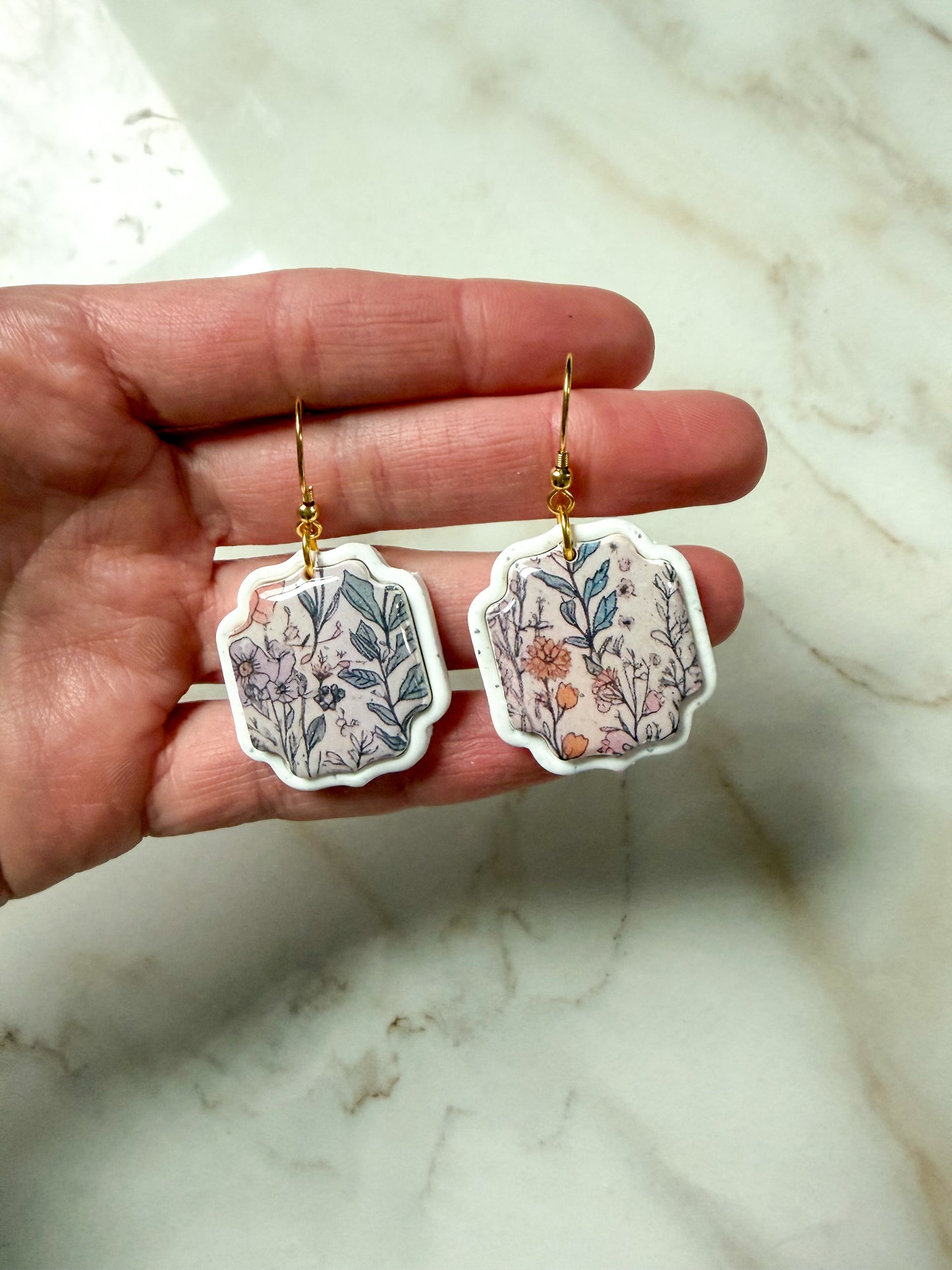 Hand holding floral earrings on a marble surface