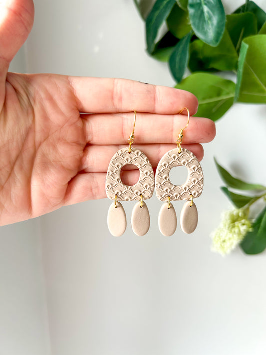 Earrings with a scalloped texture and two dangles, held in a hand 