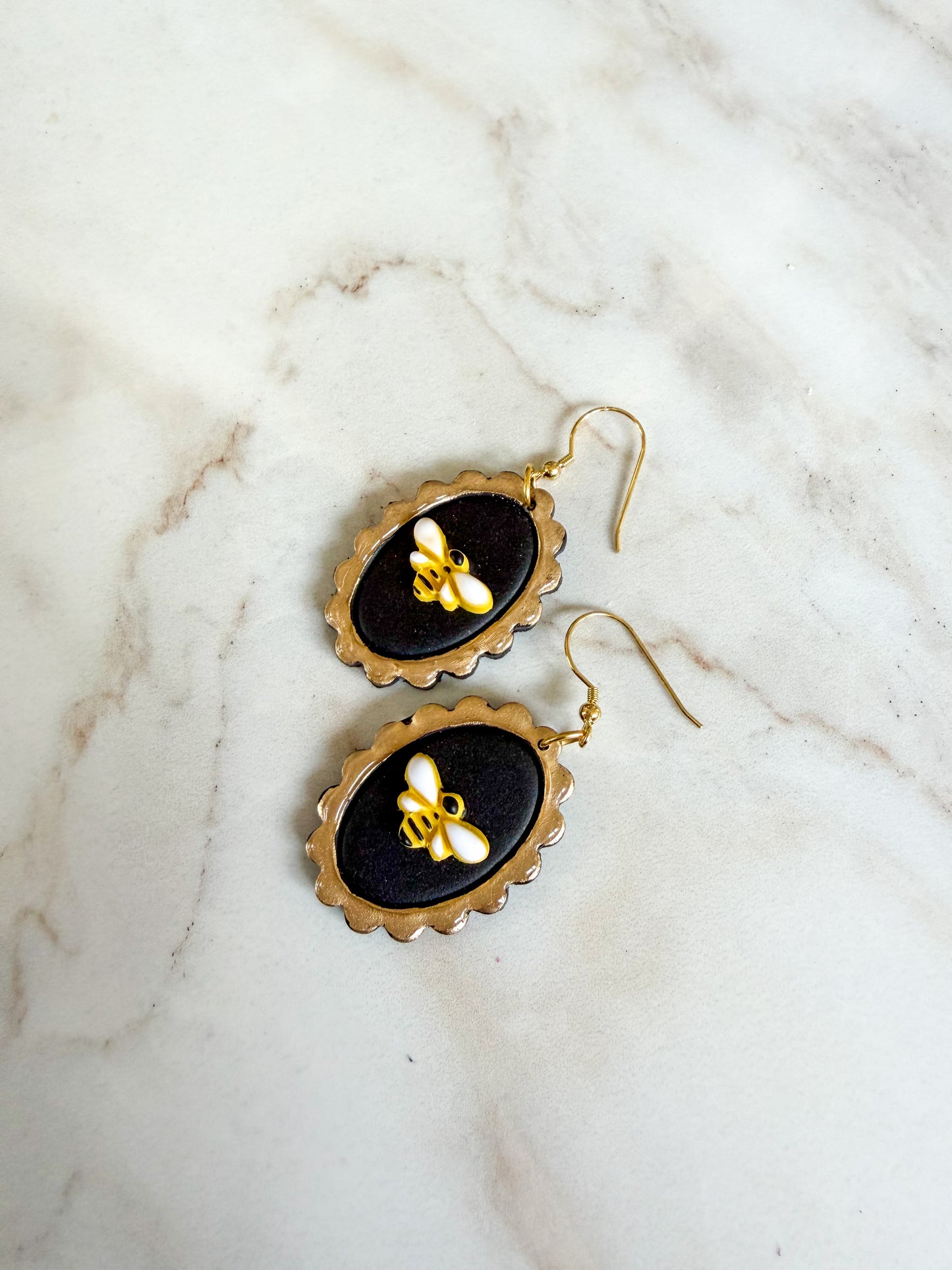 Pair of earrings with bee design on black background, displayed on marble surface