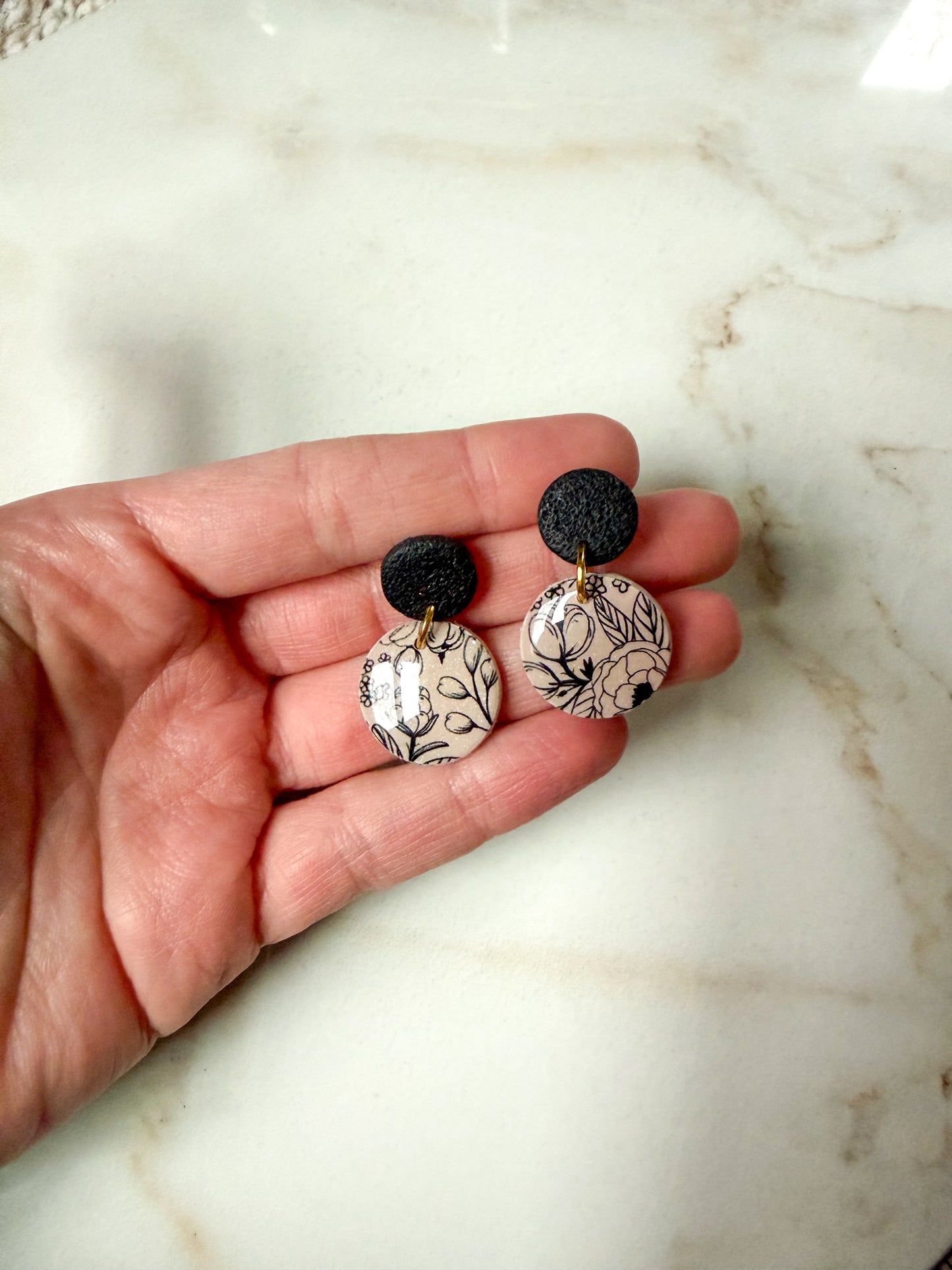 Hand holding a black and brown pair of floral earrings 