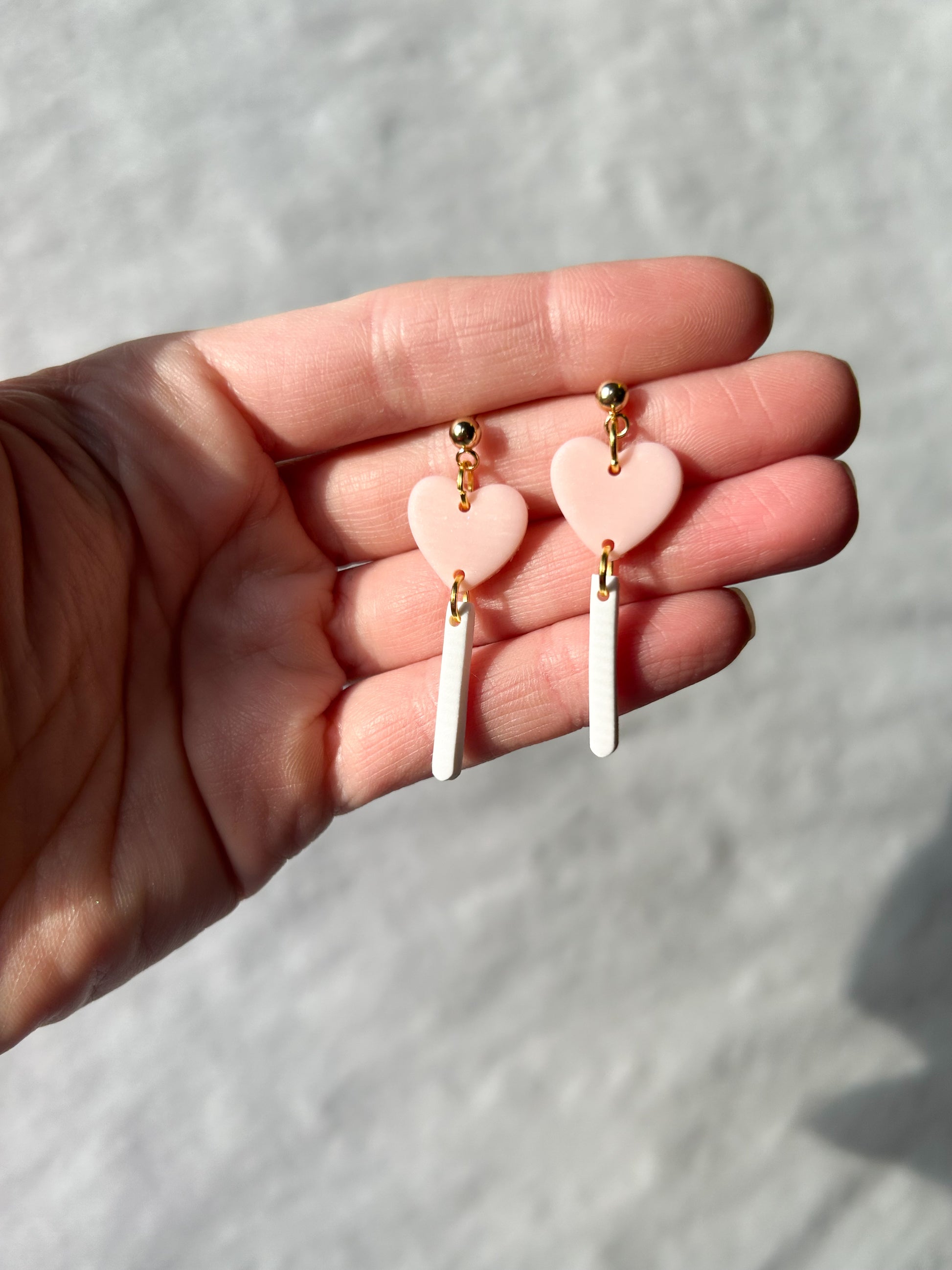 Heart-shaped earrings held in a hand against a light background