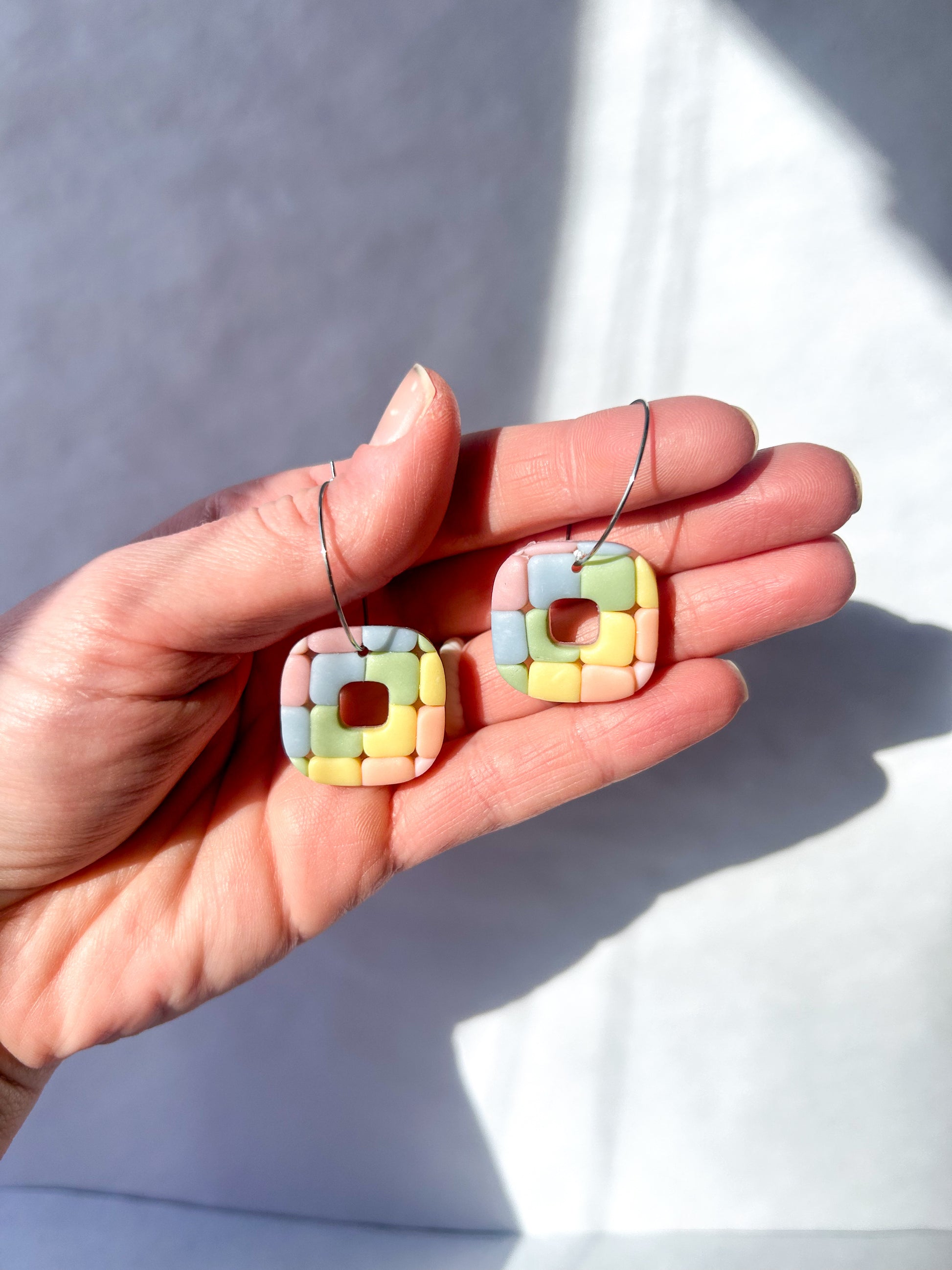 Hand holding colorful square-shaped earrings against a neutral background