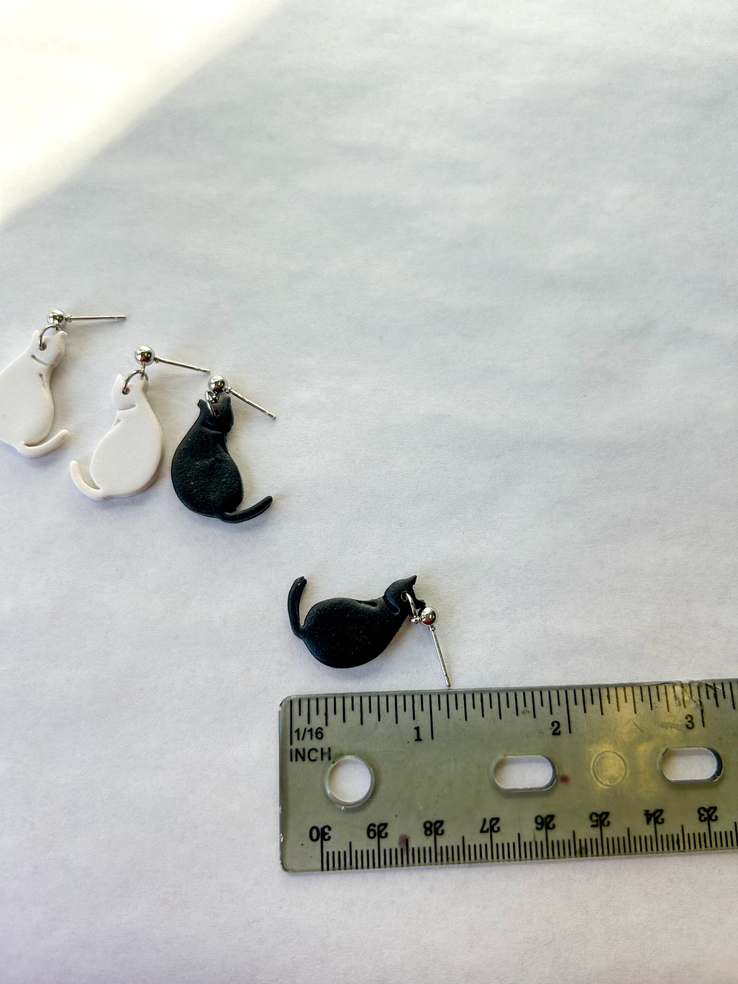 Cat-shaped earrings with a ruler for scale on a white background