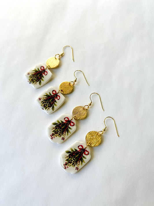 Set of earrings with bough of holly designs on them. On a white background. 
