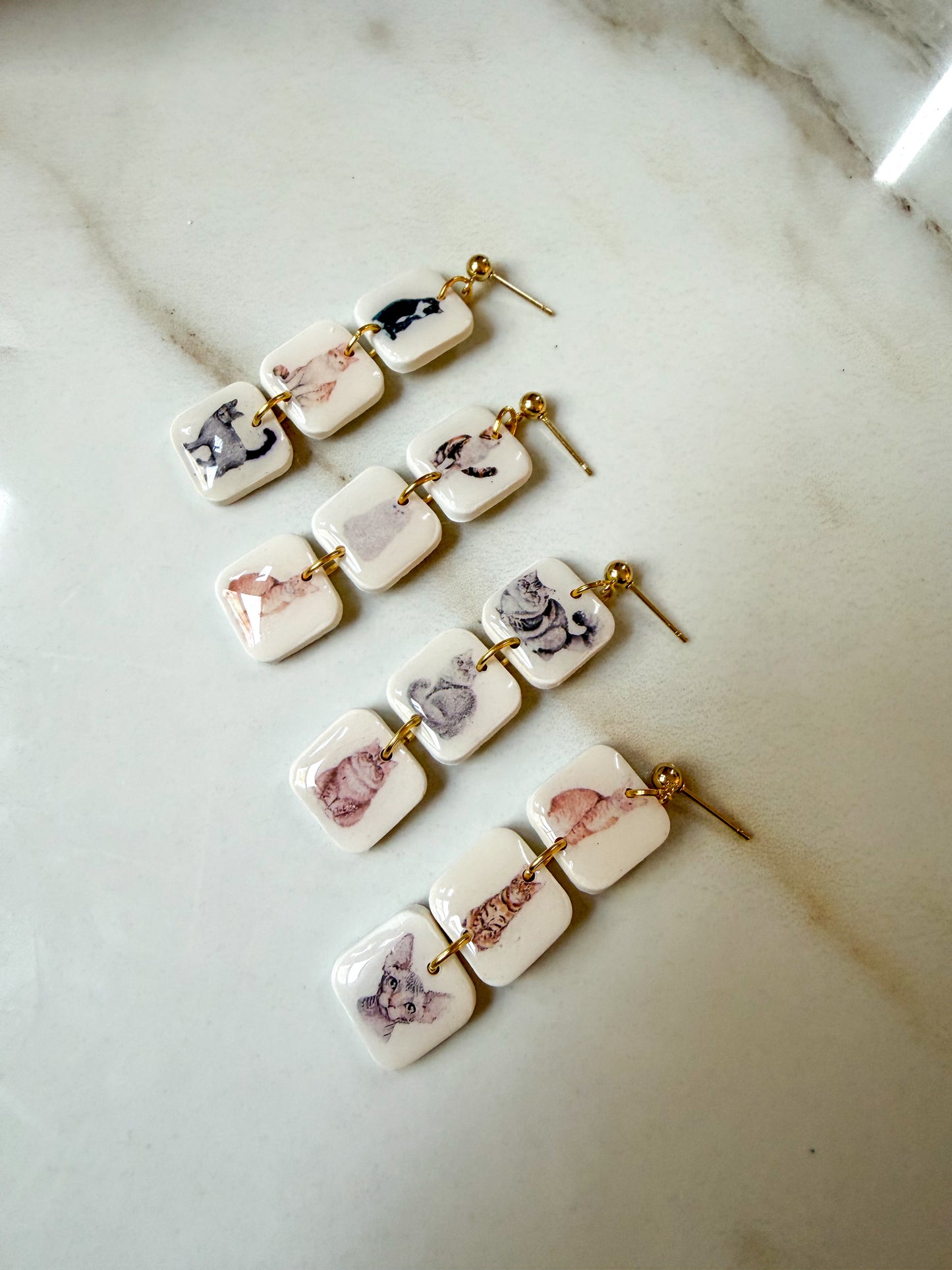 Two pairs of earrings with 3 squares on each dangle. Each square has a different cat picture in the center. The posts are hypoallergenic gold plated stainless steel. 