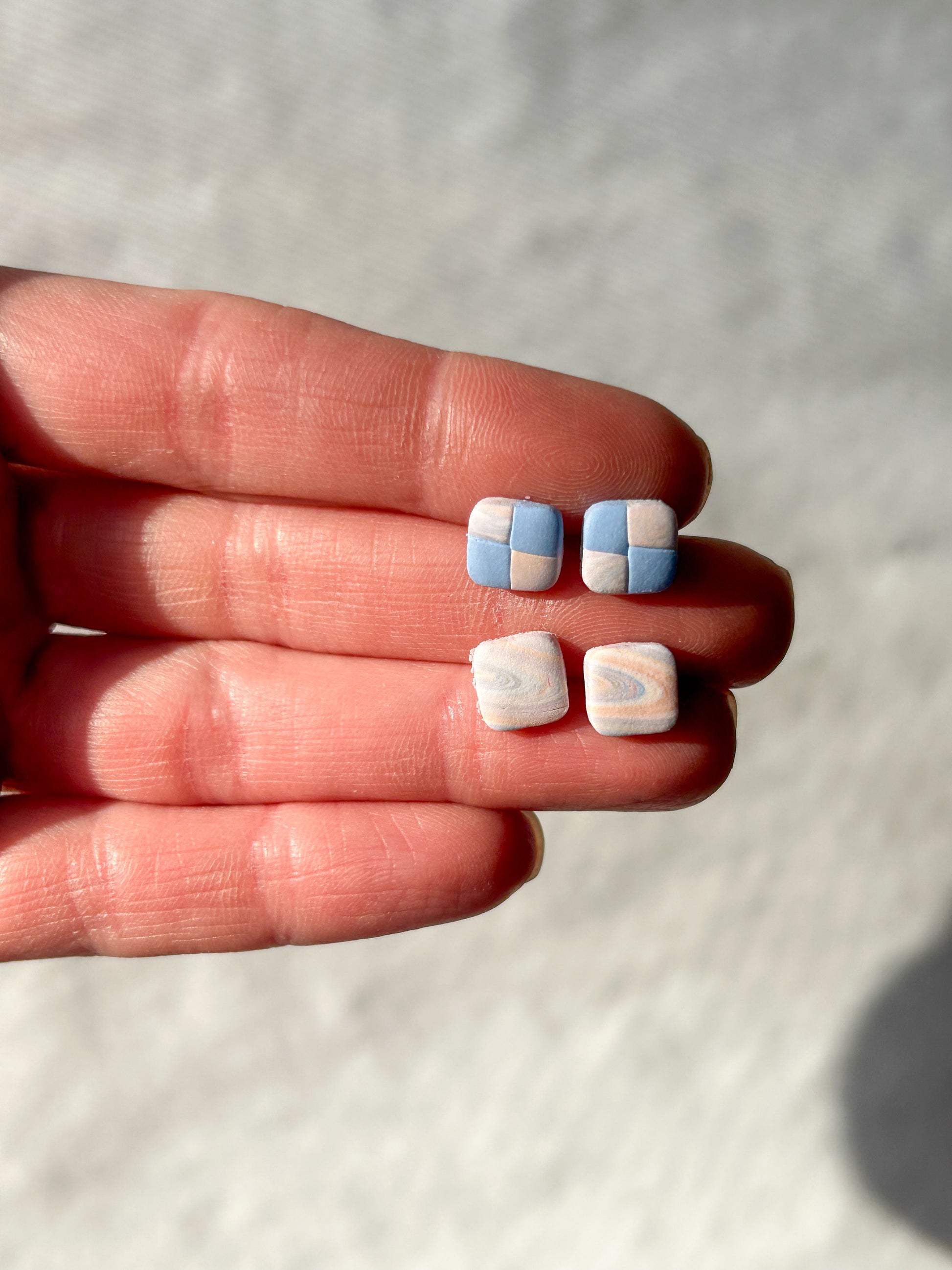 A hand holding two pairs of stud earrings