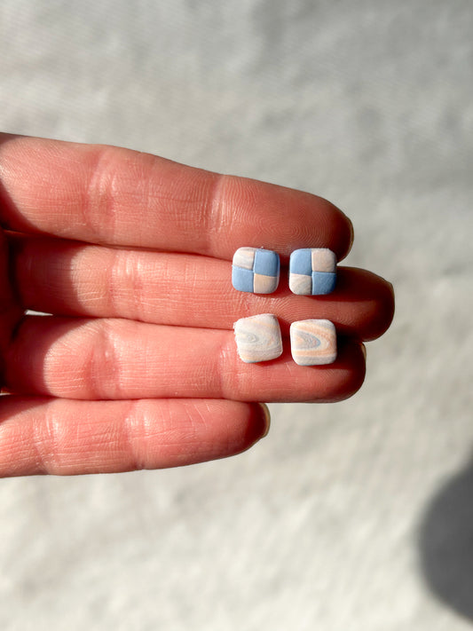 A hand holding two pairs of stud earrings