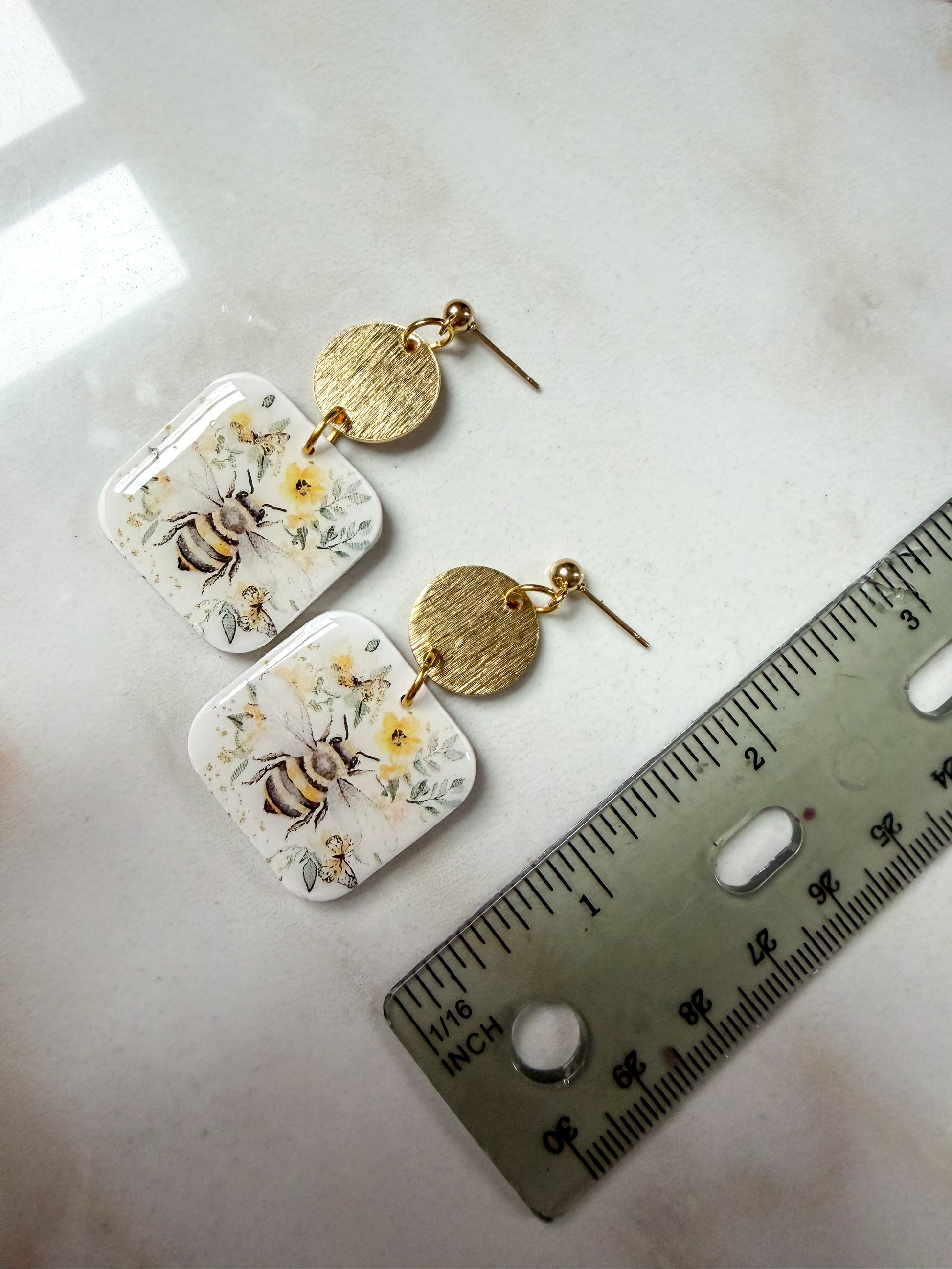 Pair of floral earrings with gold accents on a white surface next to a ruler for scale. 2 inches long. 