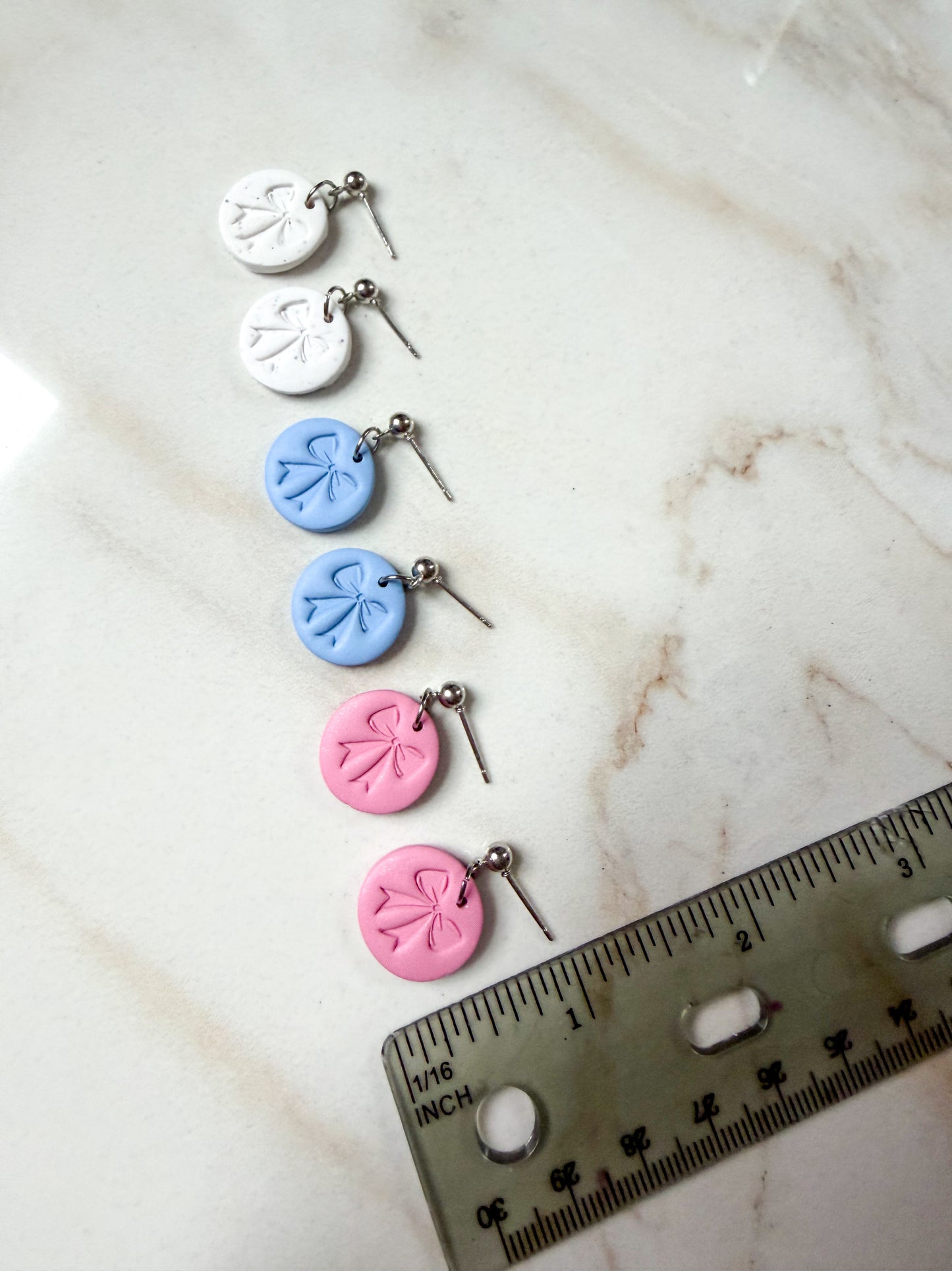 Set of colorful earrings on a marble surface with a ruler for scale. Less than 1 inch long