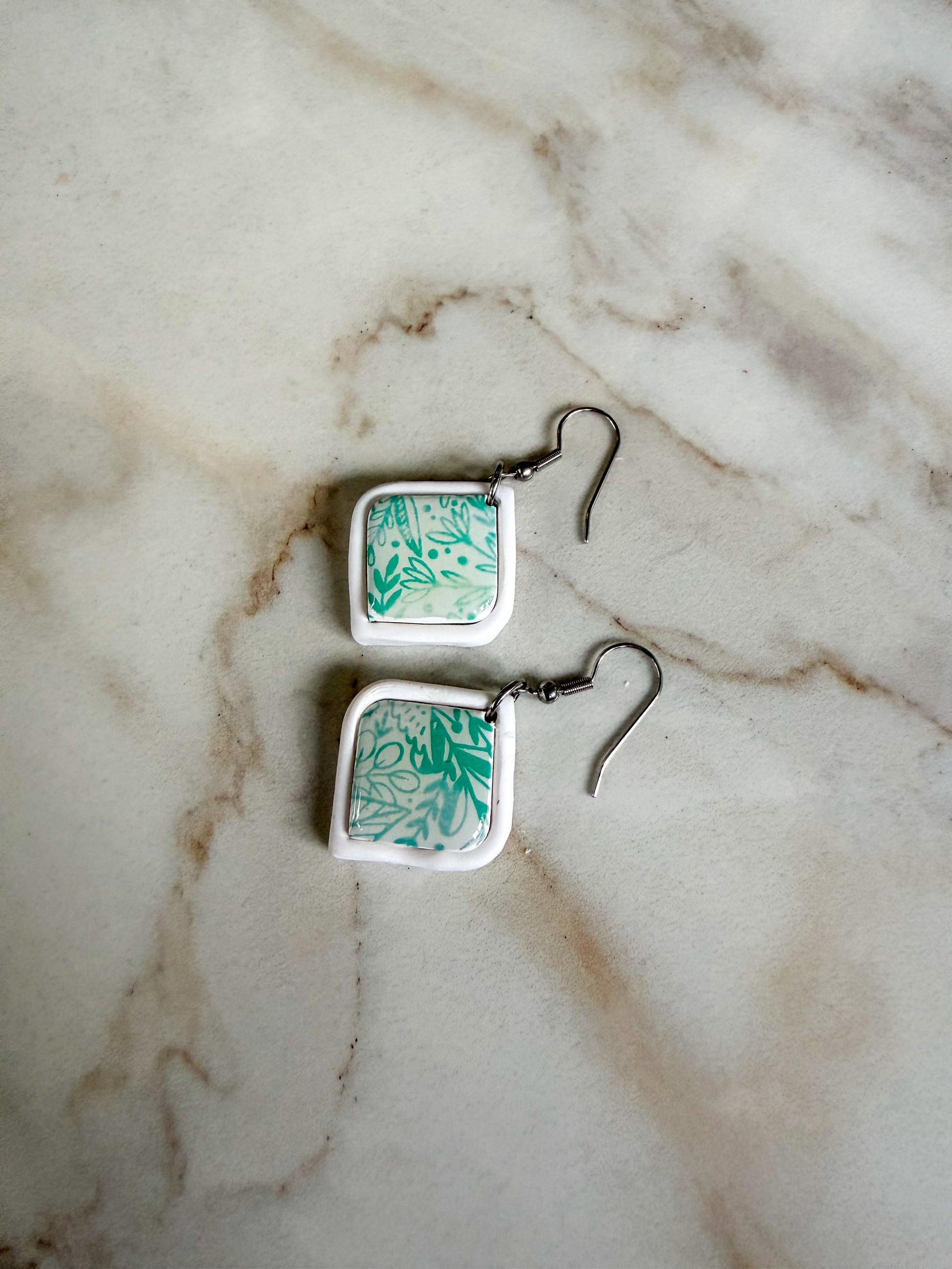 Square earrings with green floral pattern on a marble surface