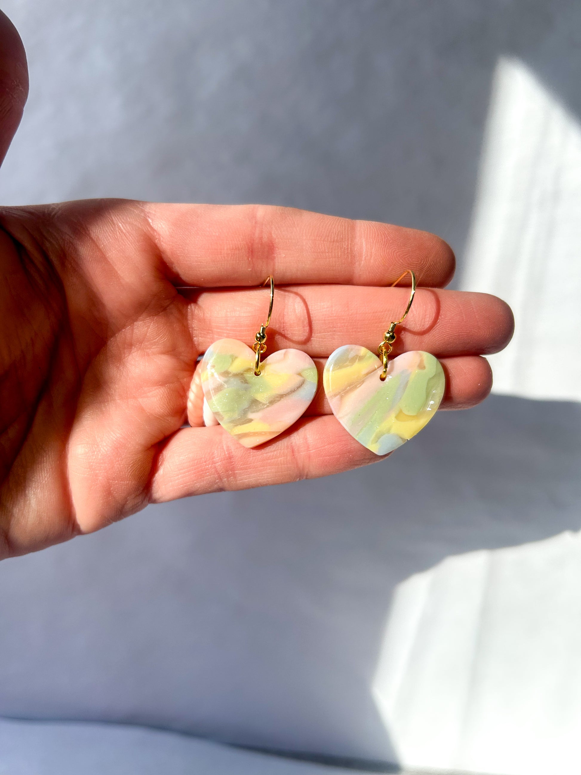 Heart-shaped earrings held in a hand against a light background