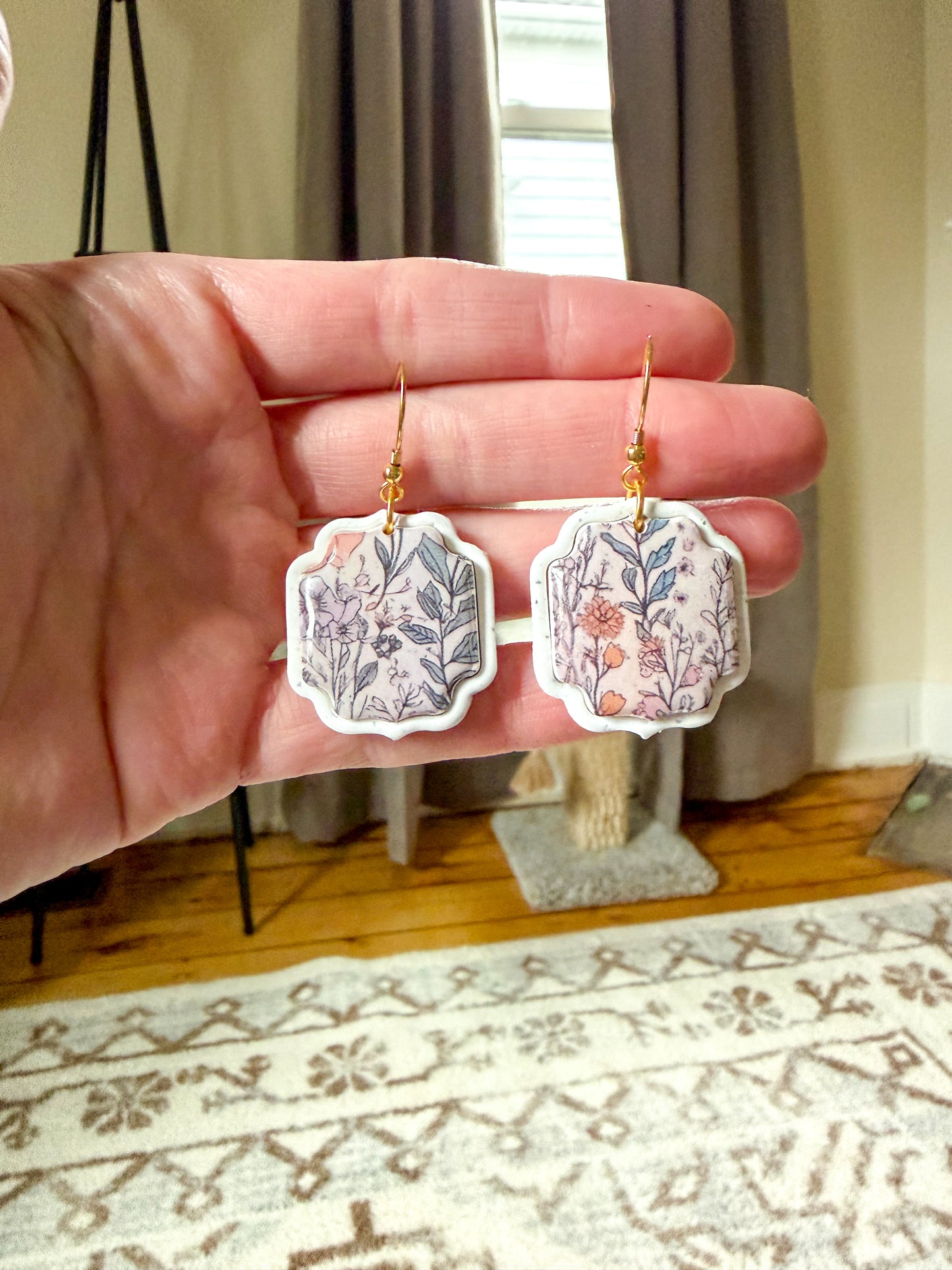 Hand holding a pair of floral earrings with a home interior background
