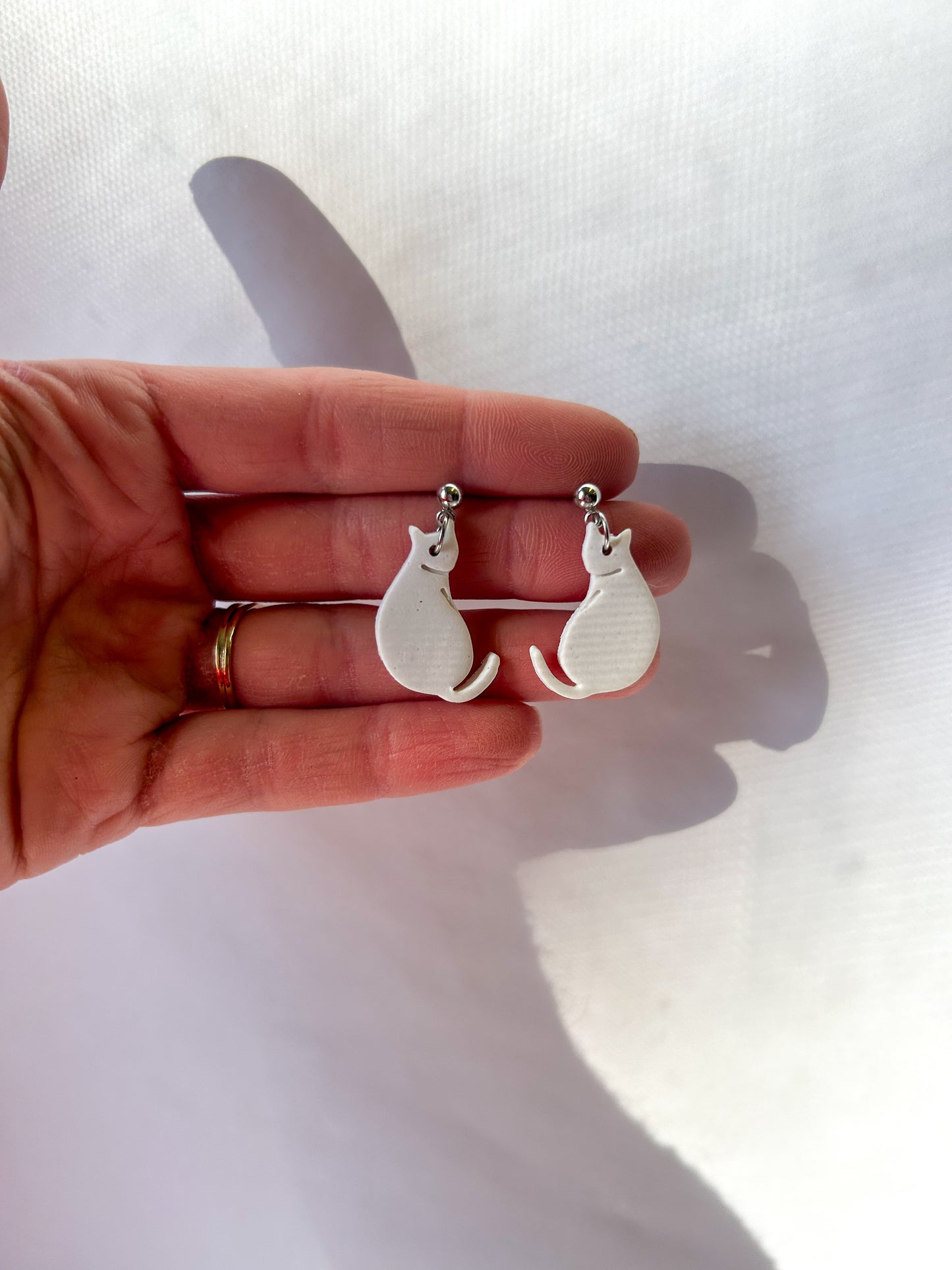 Silver cat-shaped earrings held in a hand against a white background