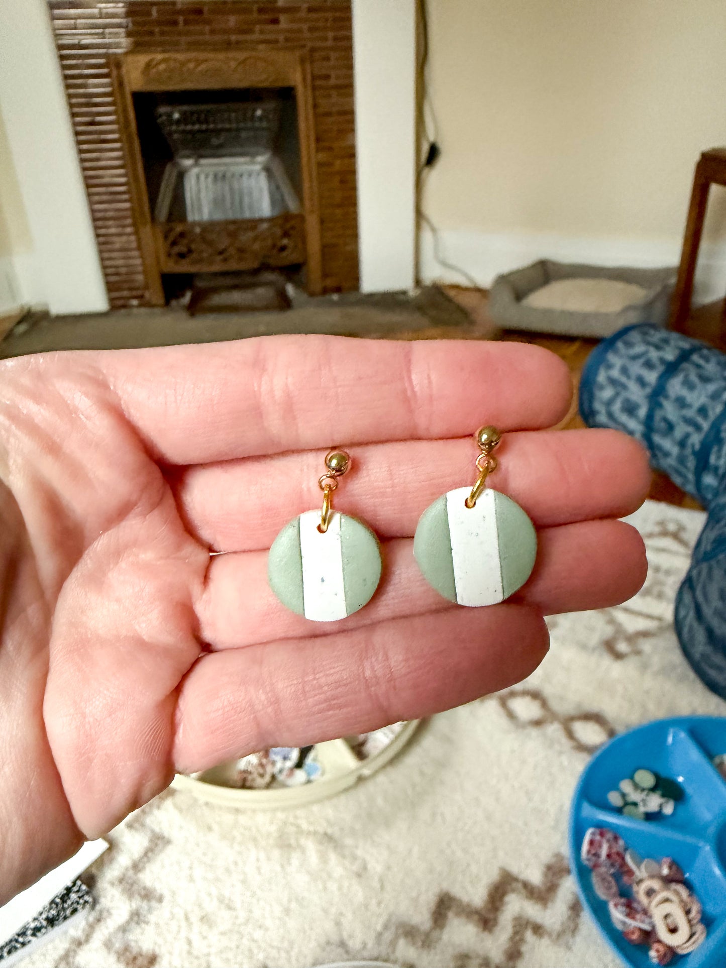 Hand holding a pair of earrings with a fireplace in the background